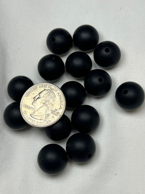 Fifteen 15mm black silicone beads with holes are arranged on a white surface.