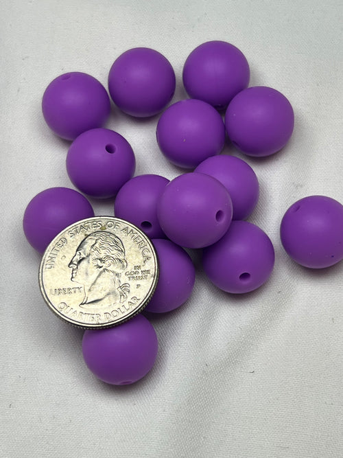 Fifteen 15mm purple silicone beads with a 2mm hole, shown with a quarter.