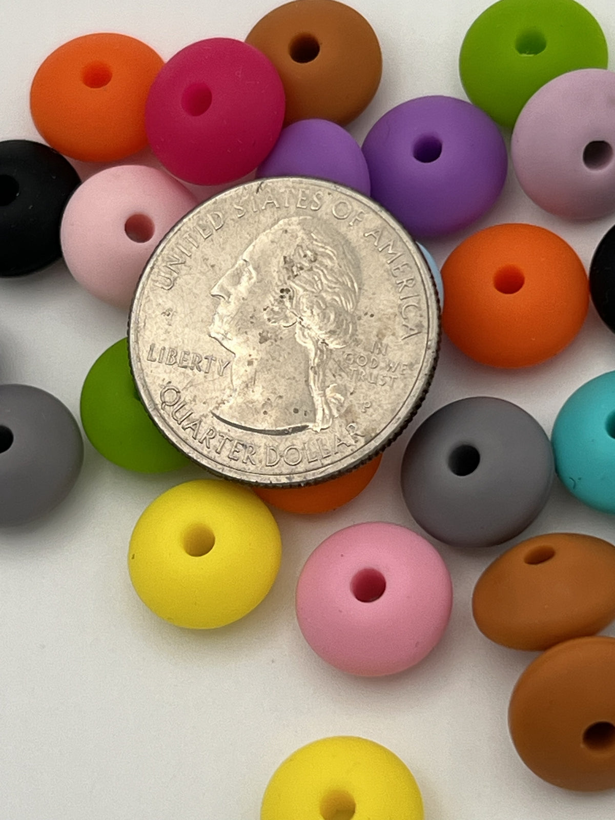 A mix of colorful 12mm silicone abacus beads shown next to a US quarter for scale.
