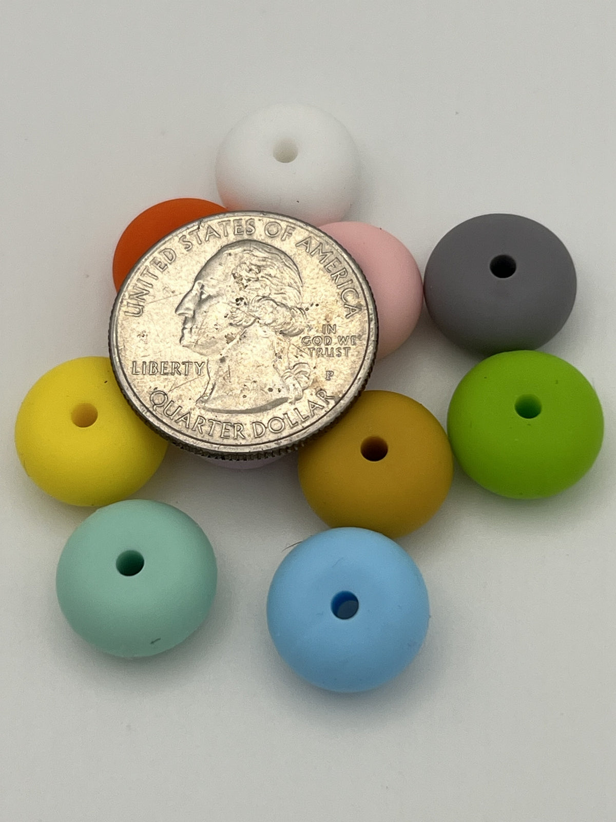 Ten 14mm silicone abacus beads in assorted colors arranged around a US quarter for size comparison.