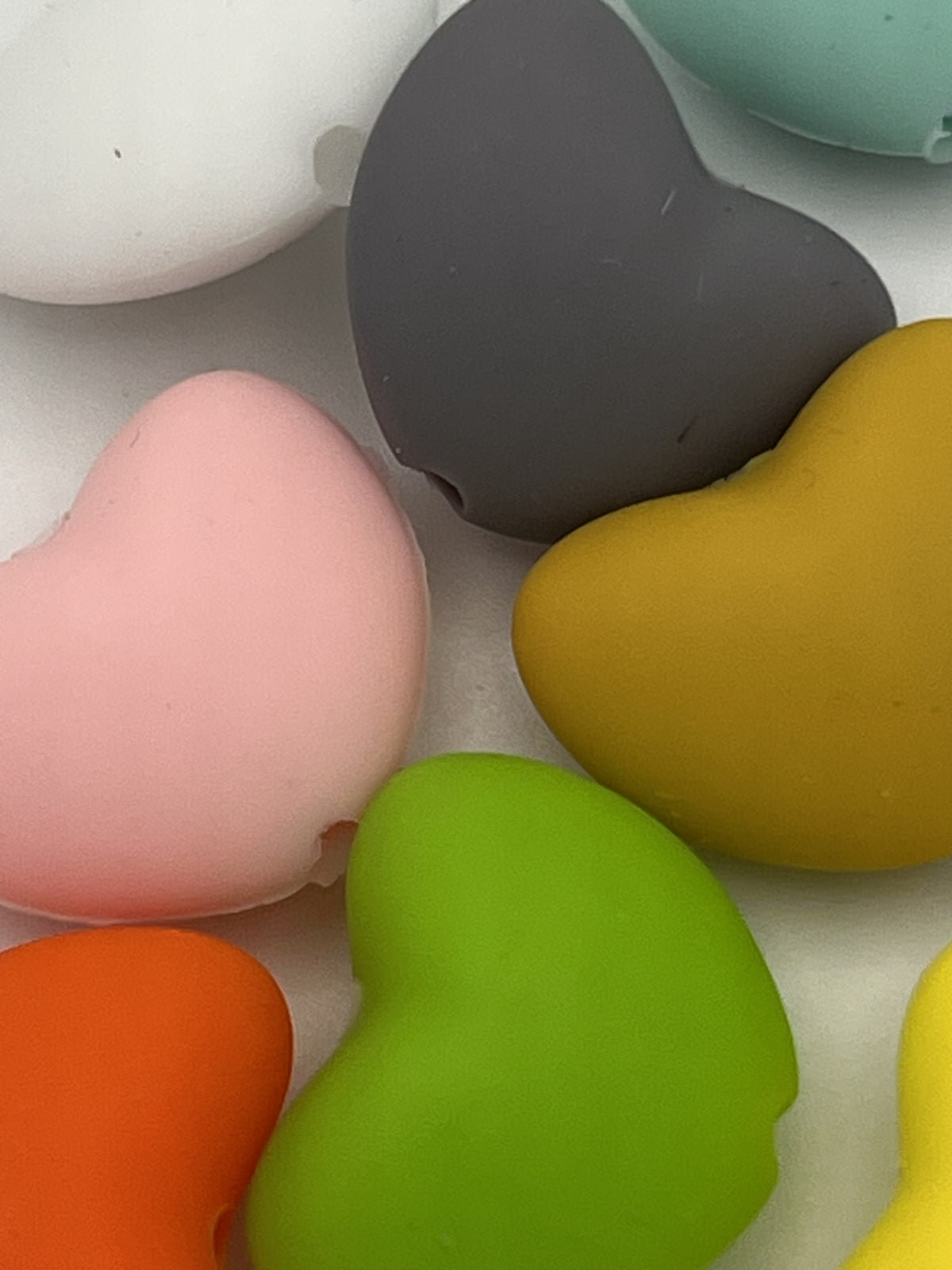 Close-up of colorful heart-shaped silicone beads in pink, green, orange, grey, and yellow.