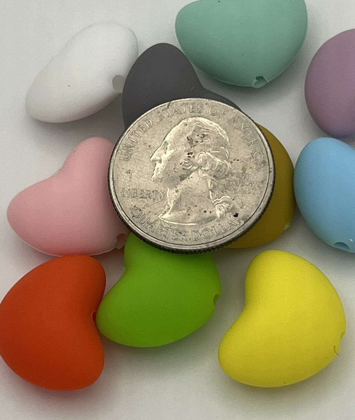 Ten colorful silicone heart beads in various shades arranged around a US quarter for scale.