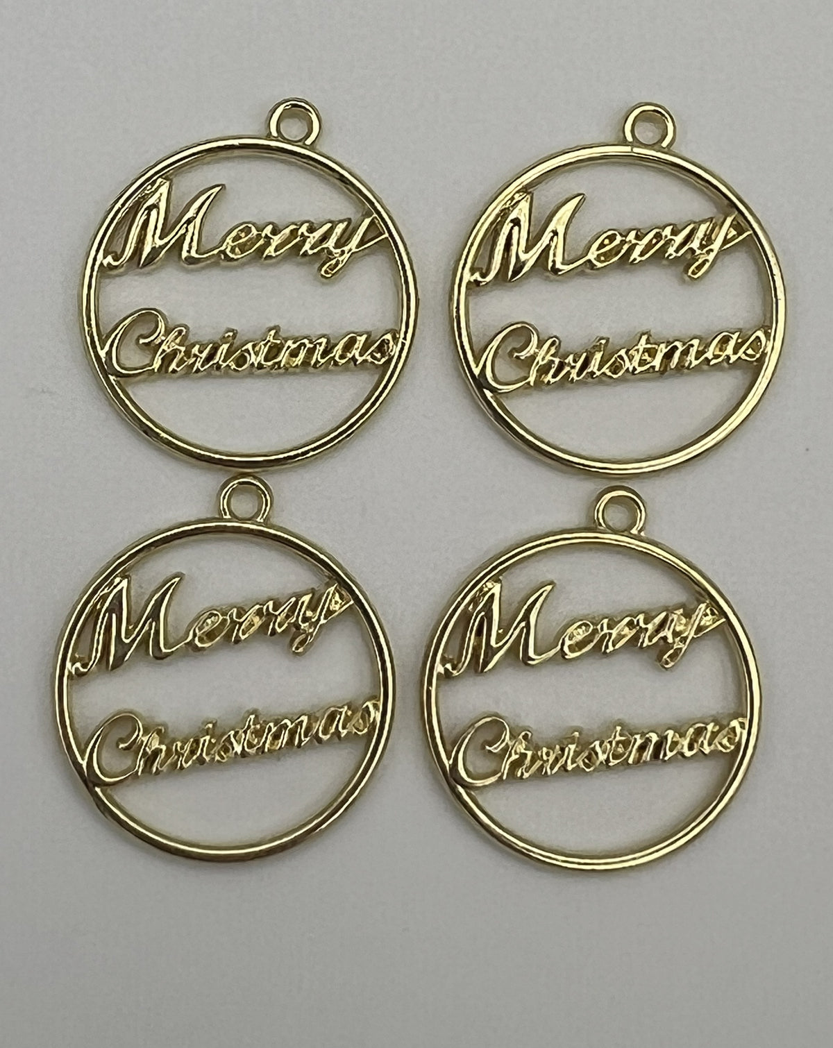 Four golden round pendants with "Merry Christmas" inscribed inside, designed for jewelry making.