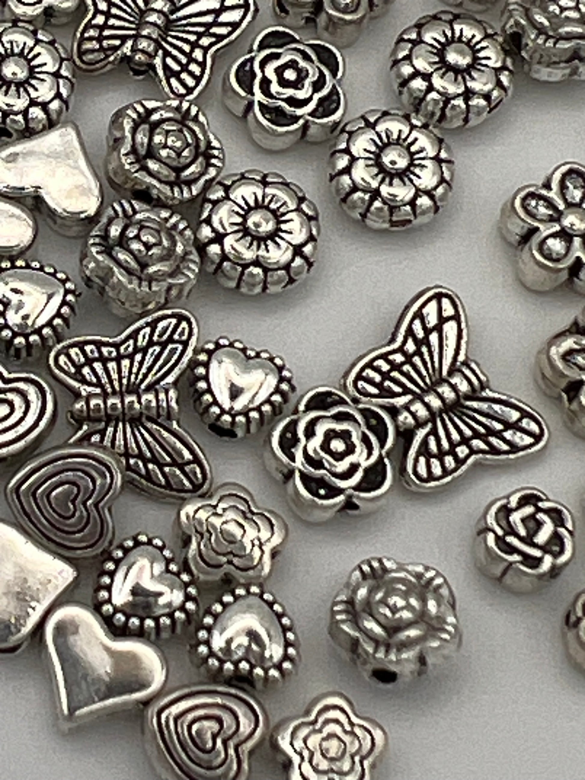 Antique silver Tibetan style beads featuring butterflies, hearts, and flowers in various designs.