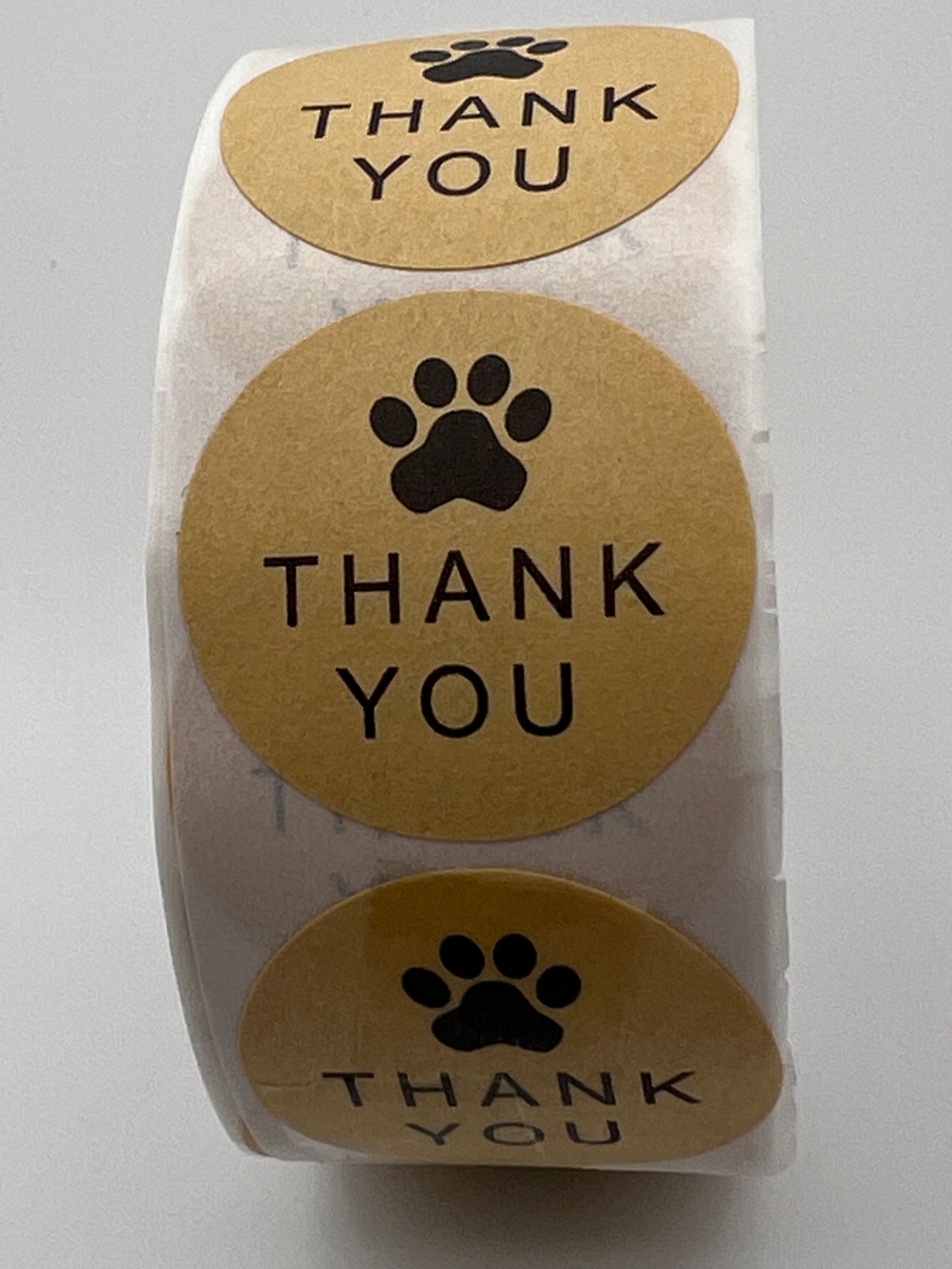 A roll of round kraft paper stickers featuring a black paw print and the words Thank You.