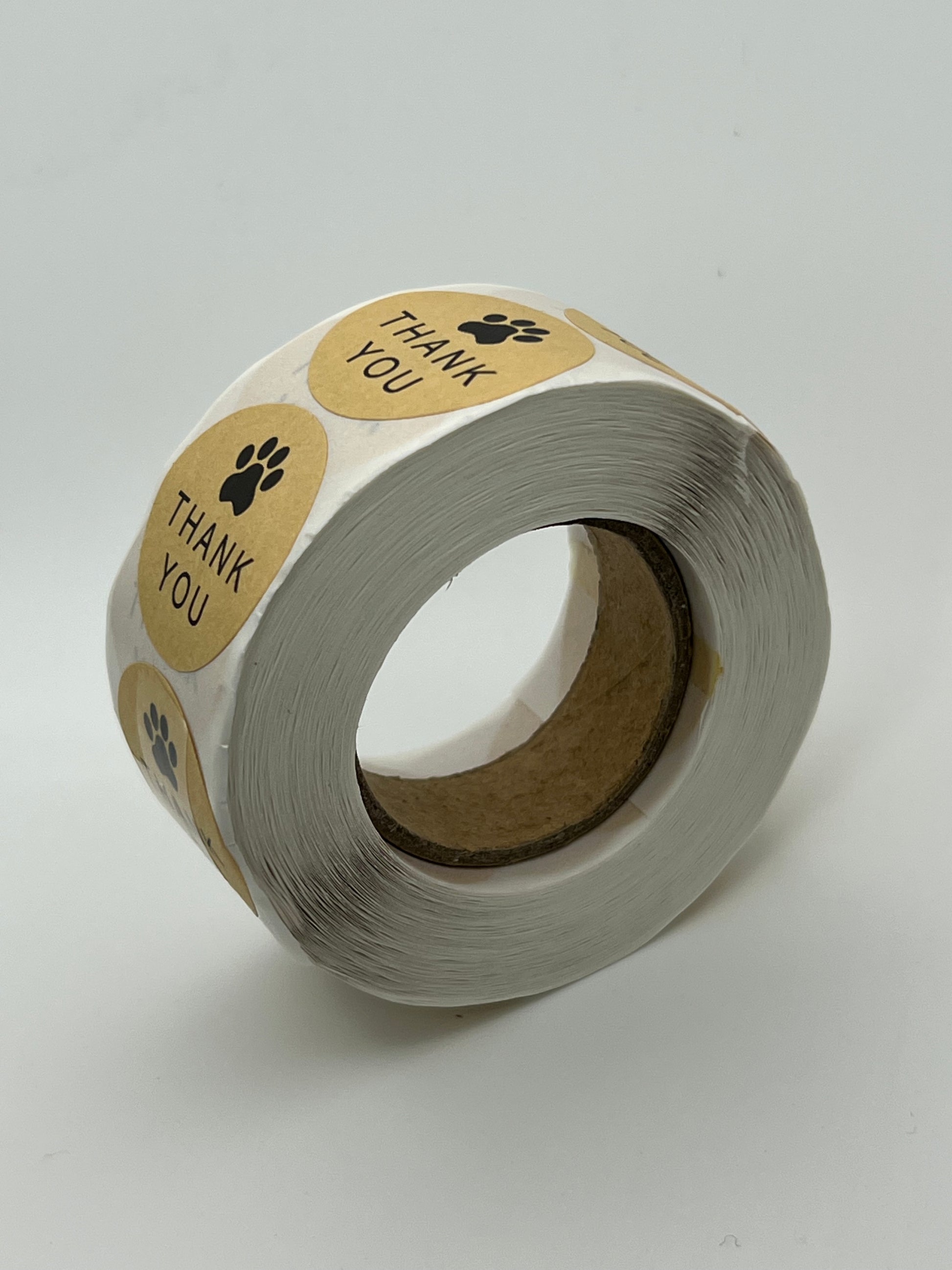 A roll of 500 round kraft brown stickers featuring a black paw print and the words Thank You.