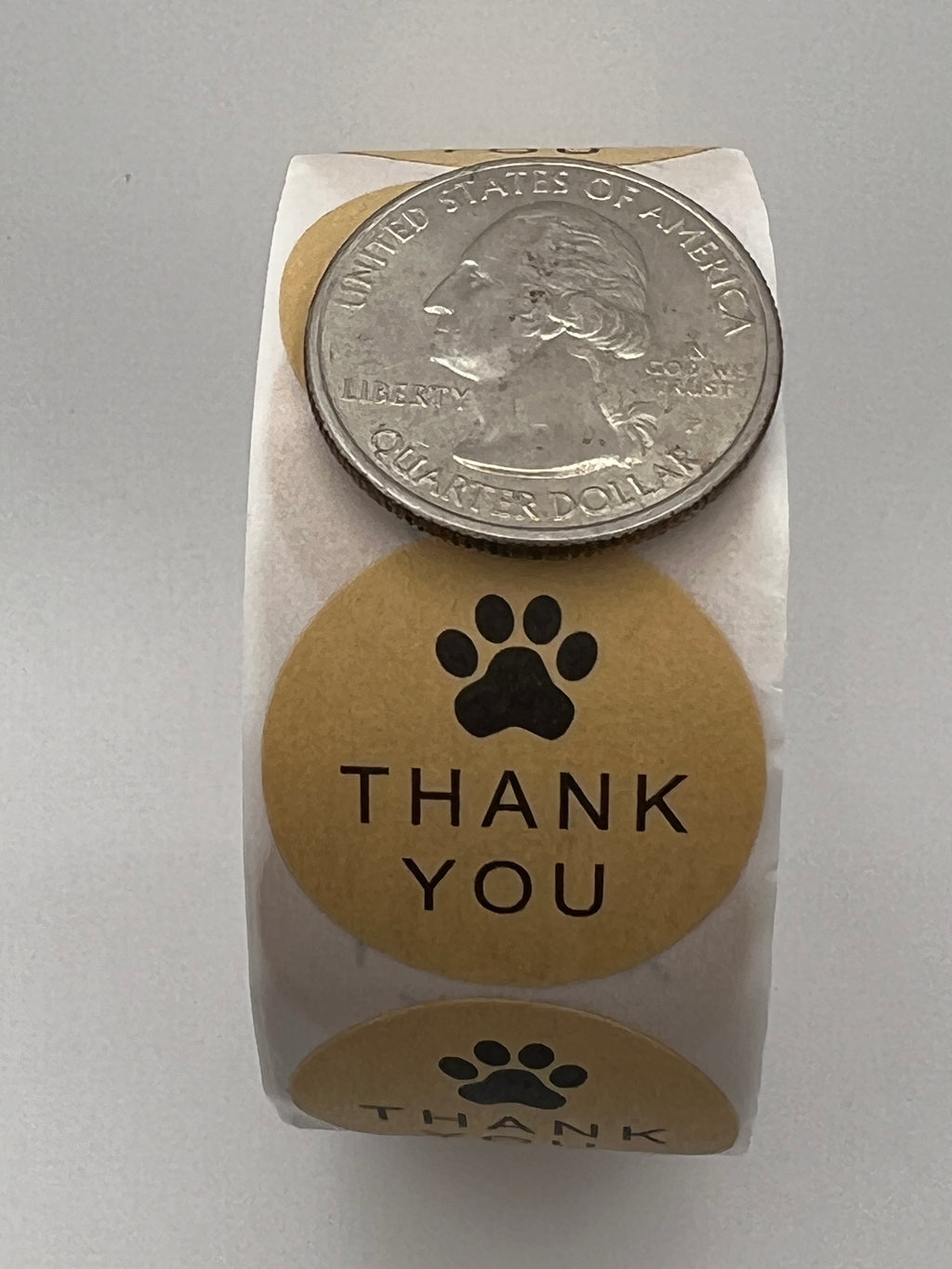 A roll of 1-inch kraft brown thank you stickers with a black paw print next to a US quarter.