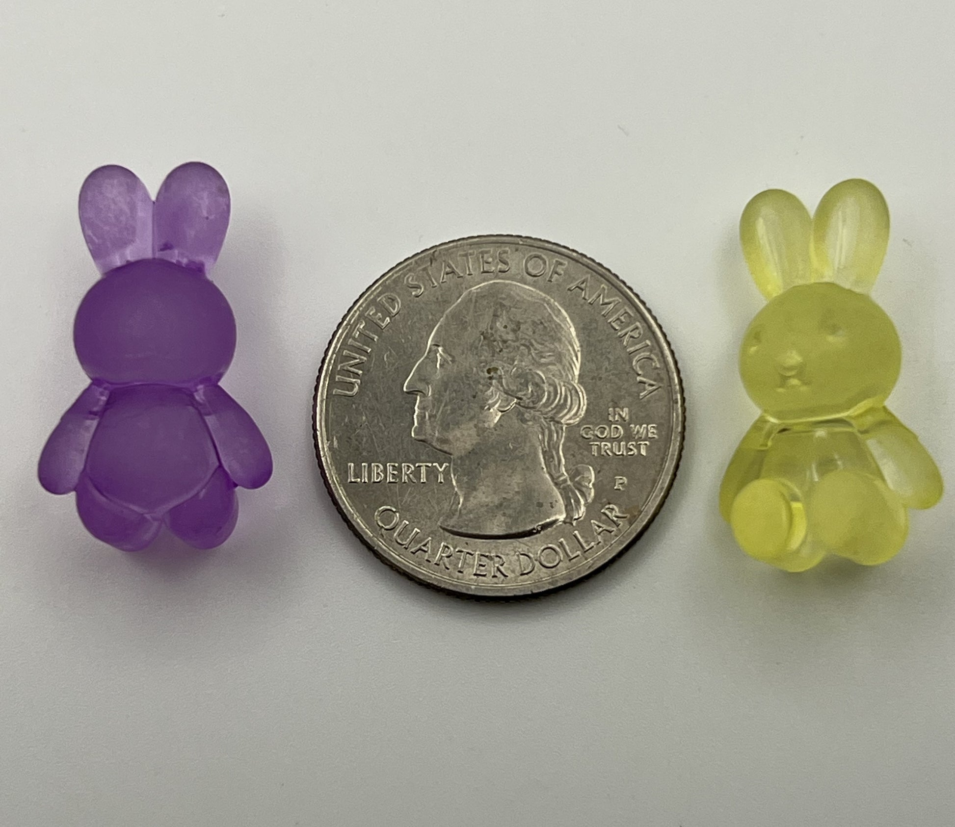Two frosted acrylic bunny beads, one purple and one yellow, sit next to a quarter.