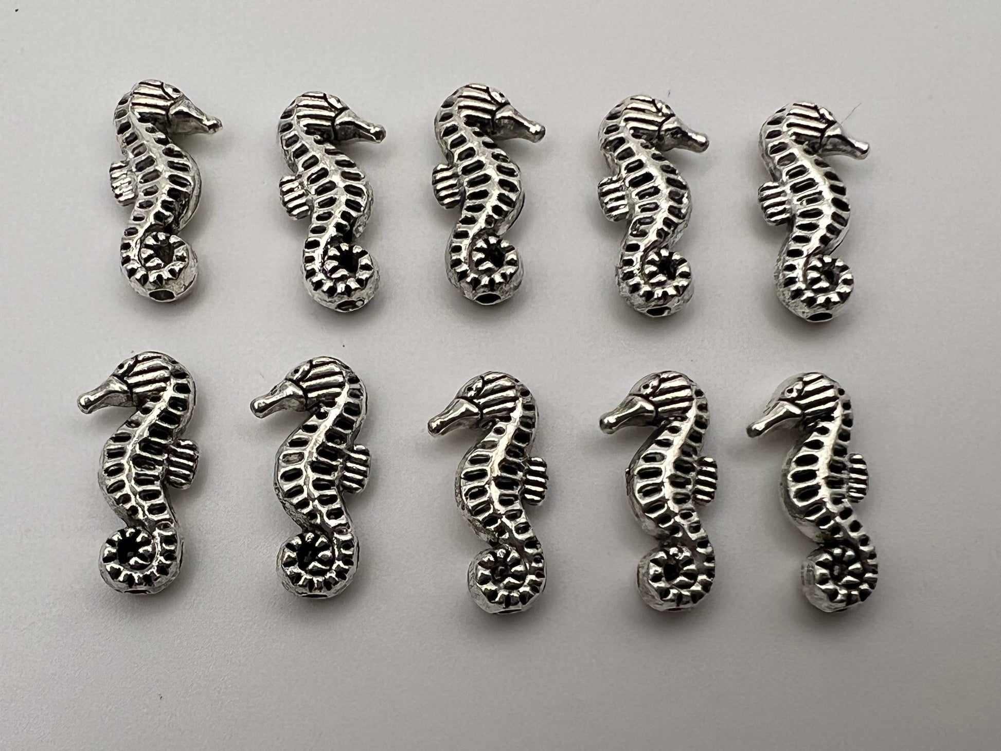 Ten antique silver seahorse beads with intricate detailing.