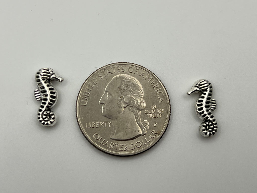 Antique silver seahorse beads with a quarter for scale.