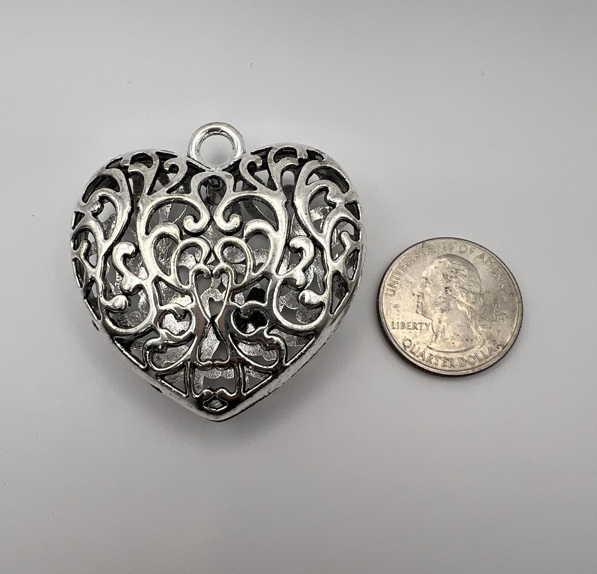 Silver Tibetan style hollow heart pendant next to a quarter.