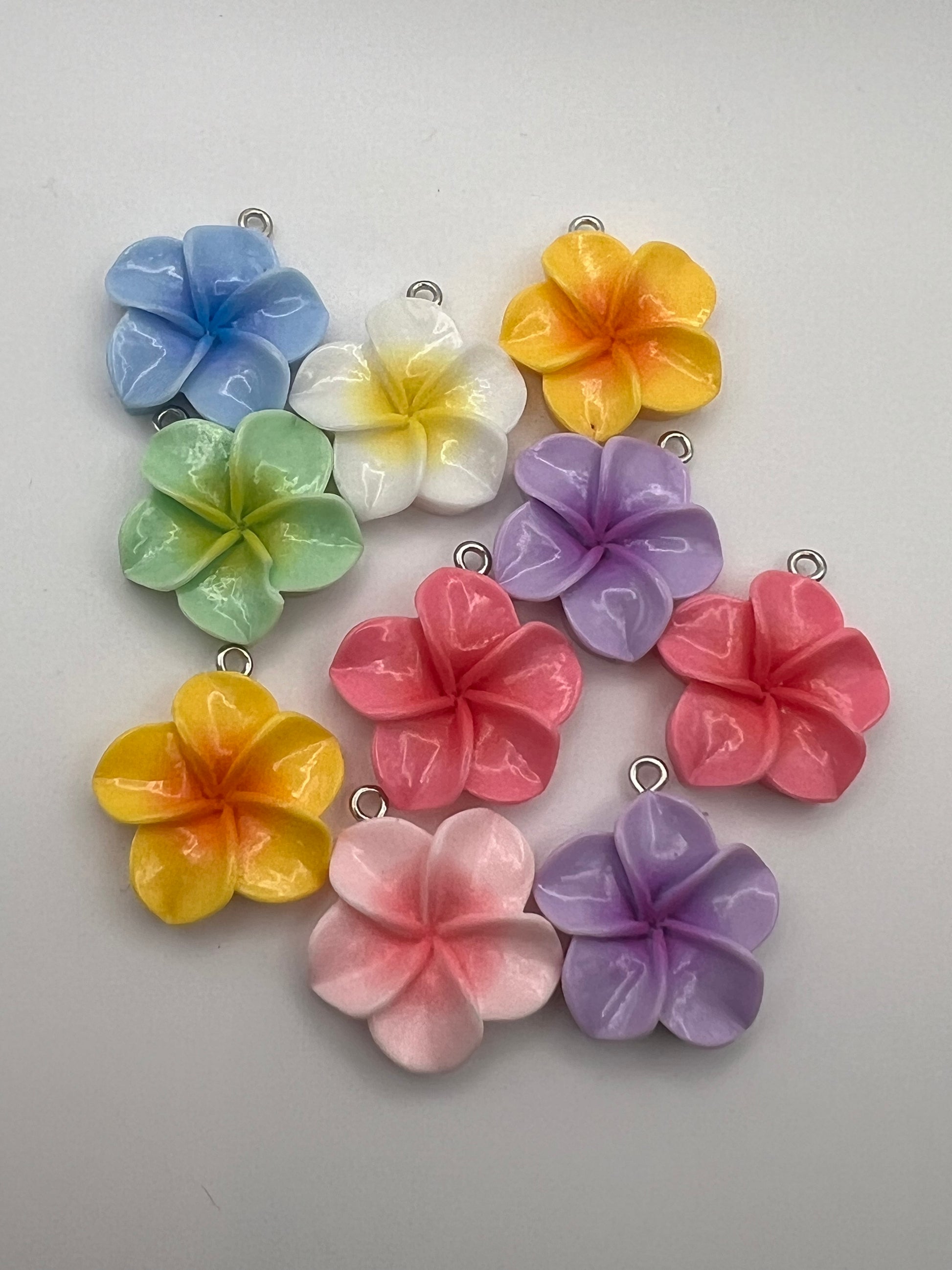 Ten mixed-color resin plumeria flower pendants with silver loops.