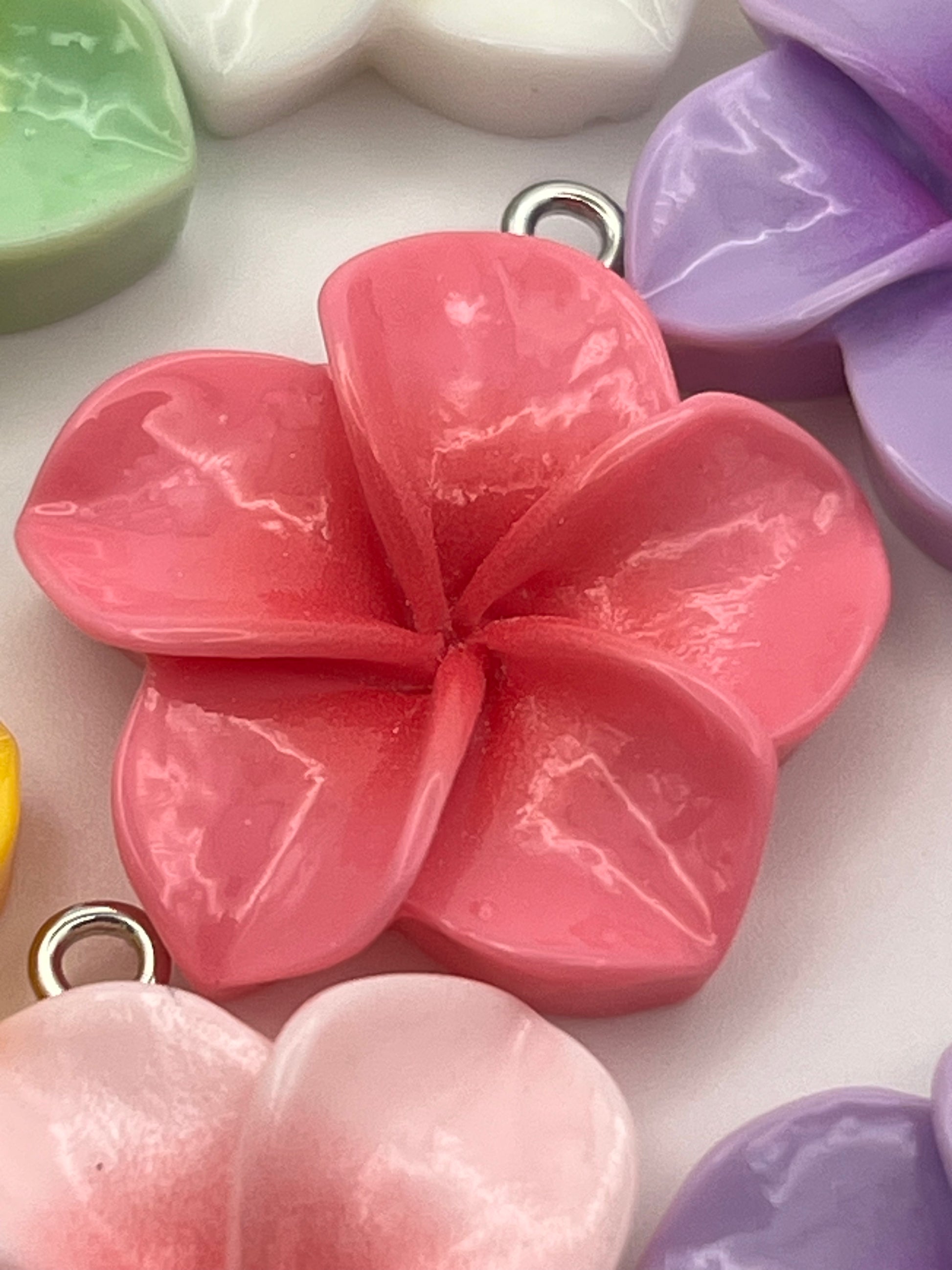 Resin plumeria flower pendants in mixed colors with metal loops.