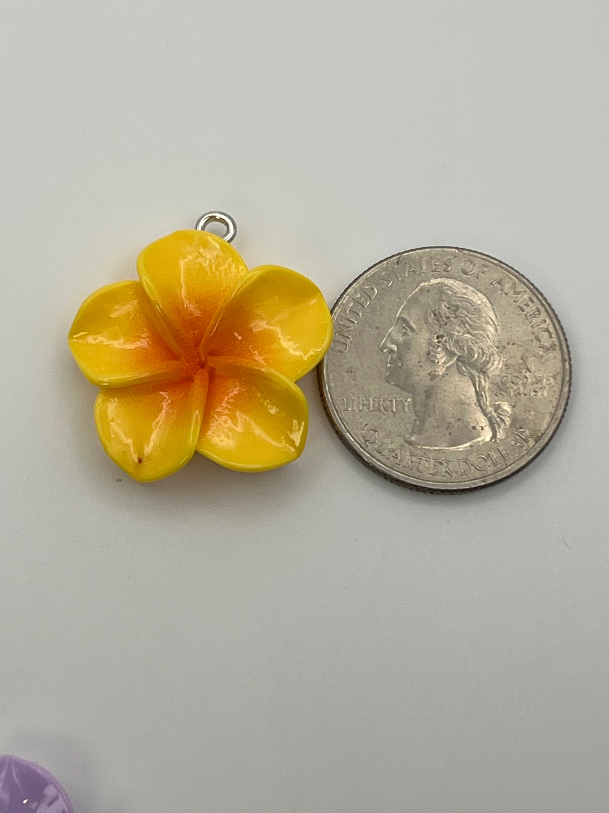 Yellow resin plumeria flower charm next to a quarter.