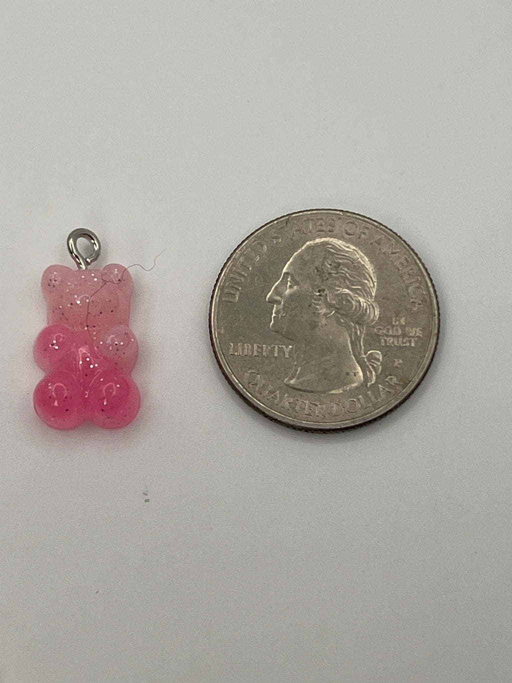 Pink glitter gummy bear charm next to a quarter.