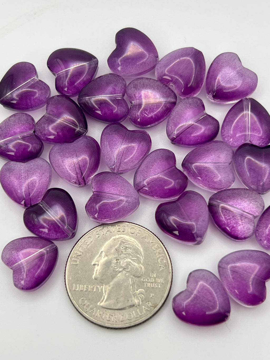 Transparent purple glass heart beads scattered around a quarter.