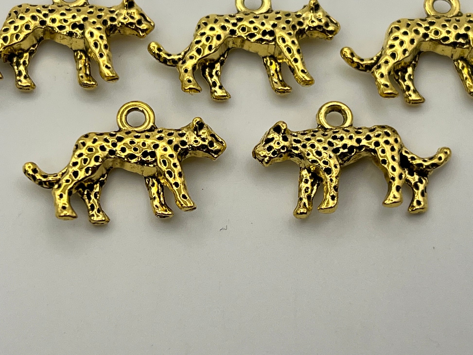 Five antique golden Tibetan style leopard charms with black spots.