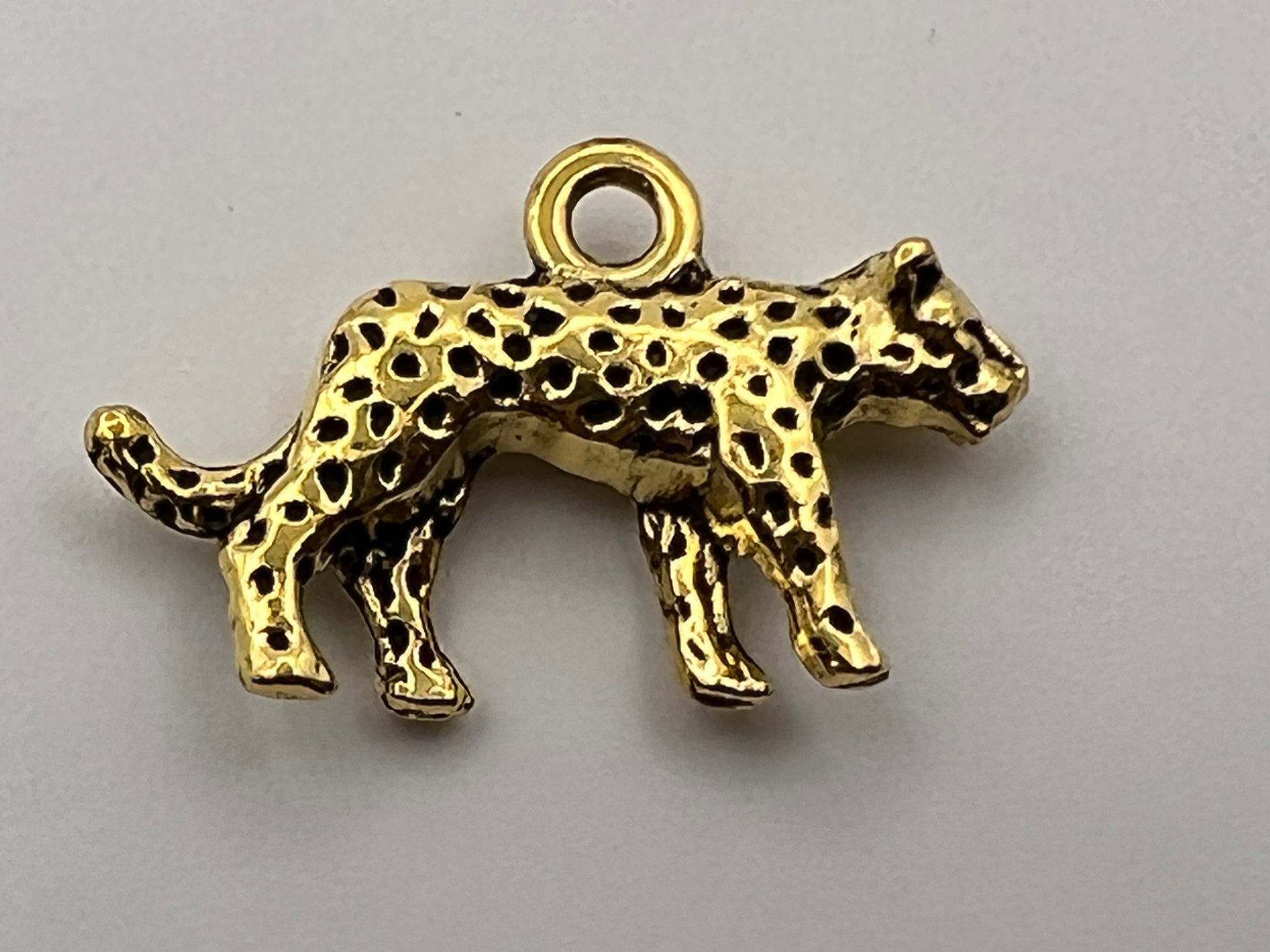 A gold-colored leopard charm with black spots and a loop for jewelry.
