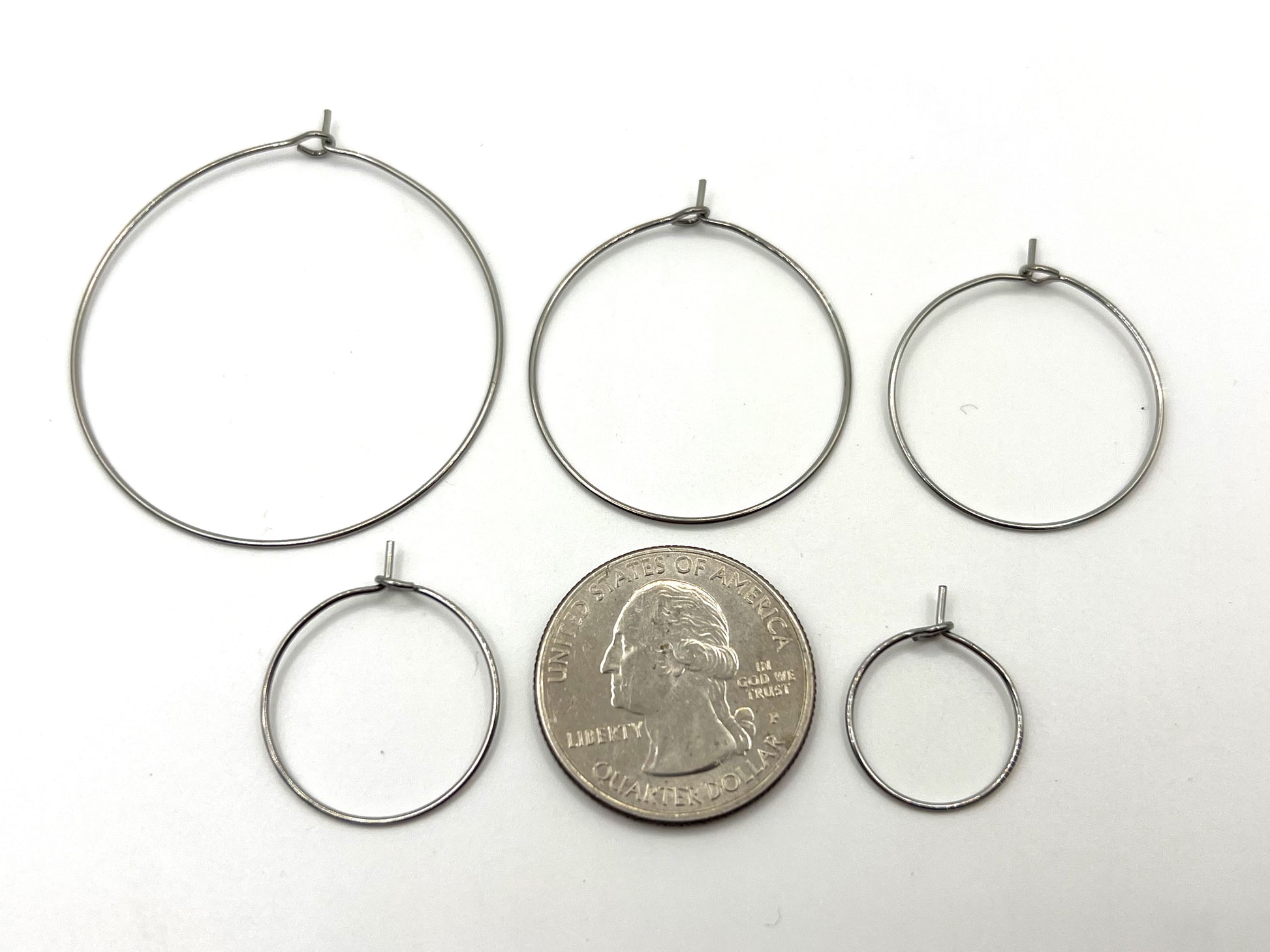 Five silver hoop earrings of varying sizes are displayed with a quarter for scale.