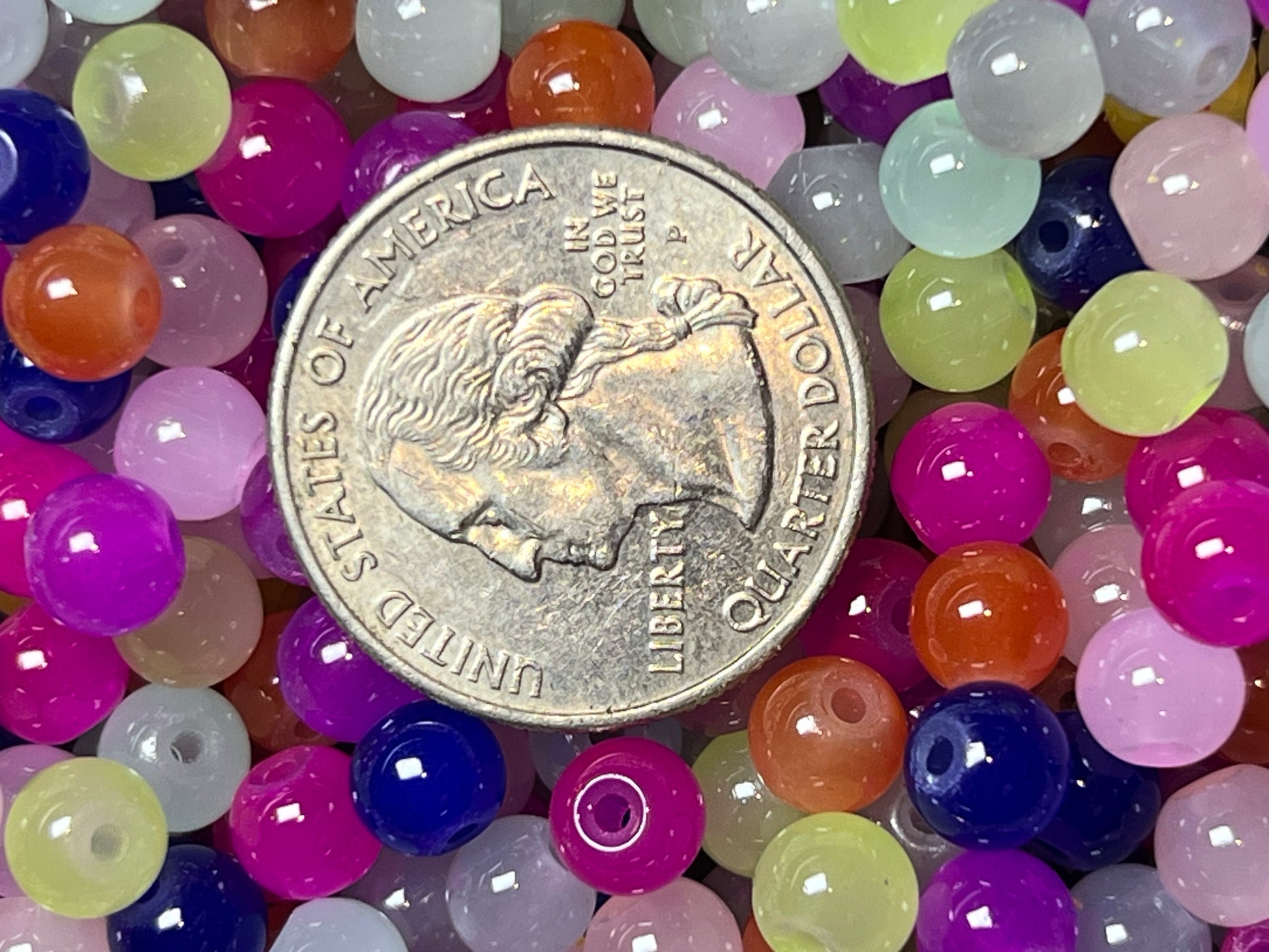 A pile of colorful 6mm glass imitation jade beads shown next to a US quarter for scale.