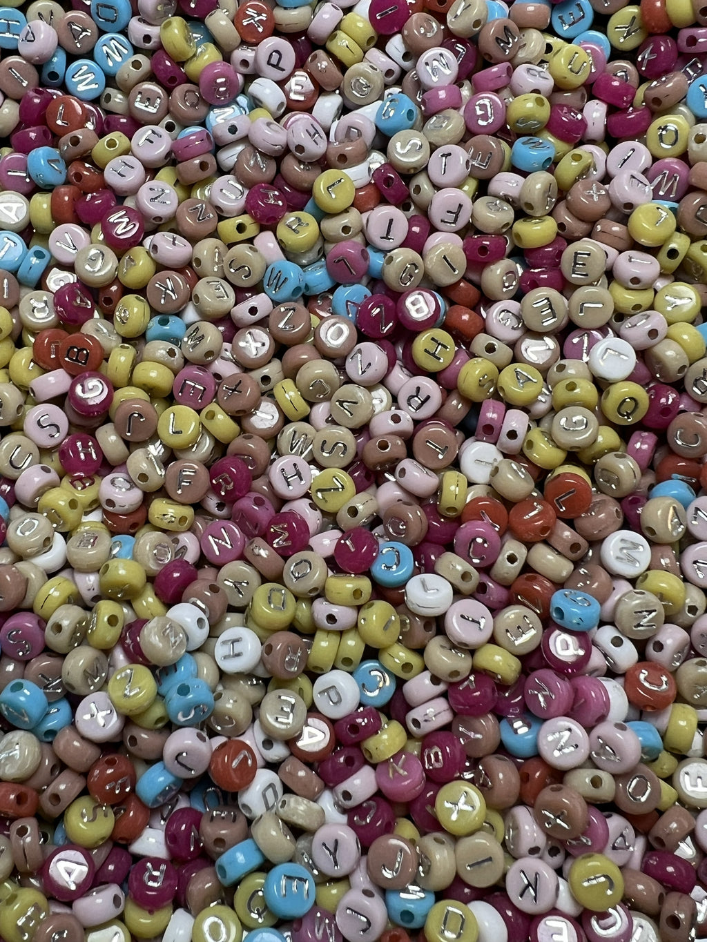 A pile of small, colorful acrylic beads featuring silver letters for jewelry making.