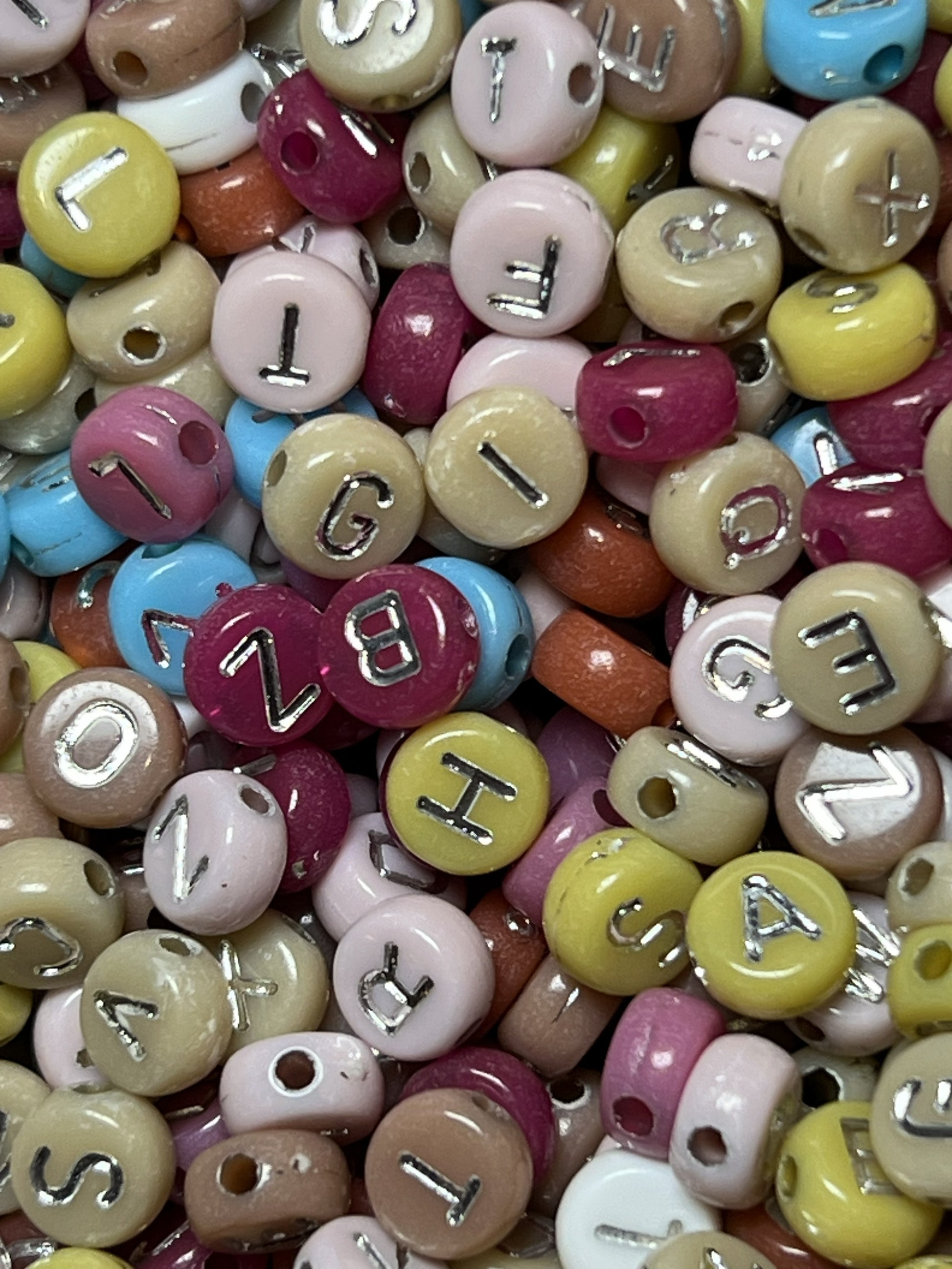 A pile of colorful acrylic beads featuring silver letters in a 7x4mm size.