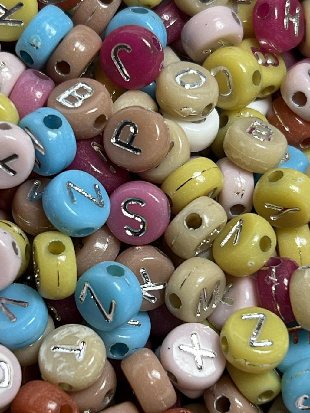 A pile of colorful acrylic beads featuring silver letters in a 7x4mm size.