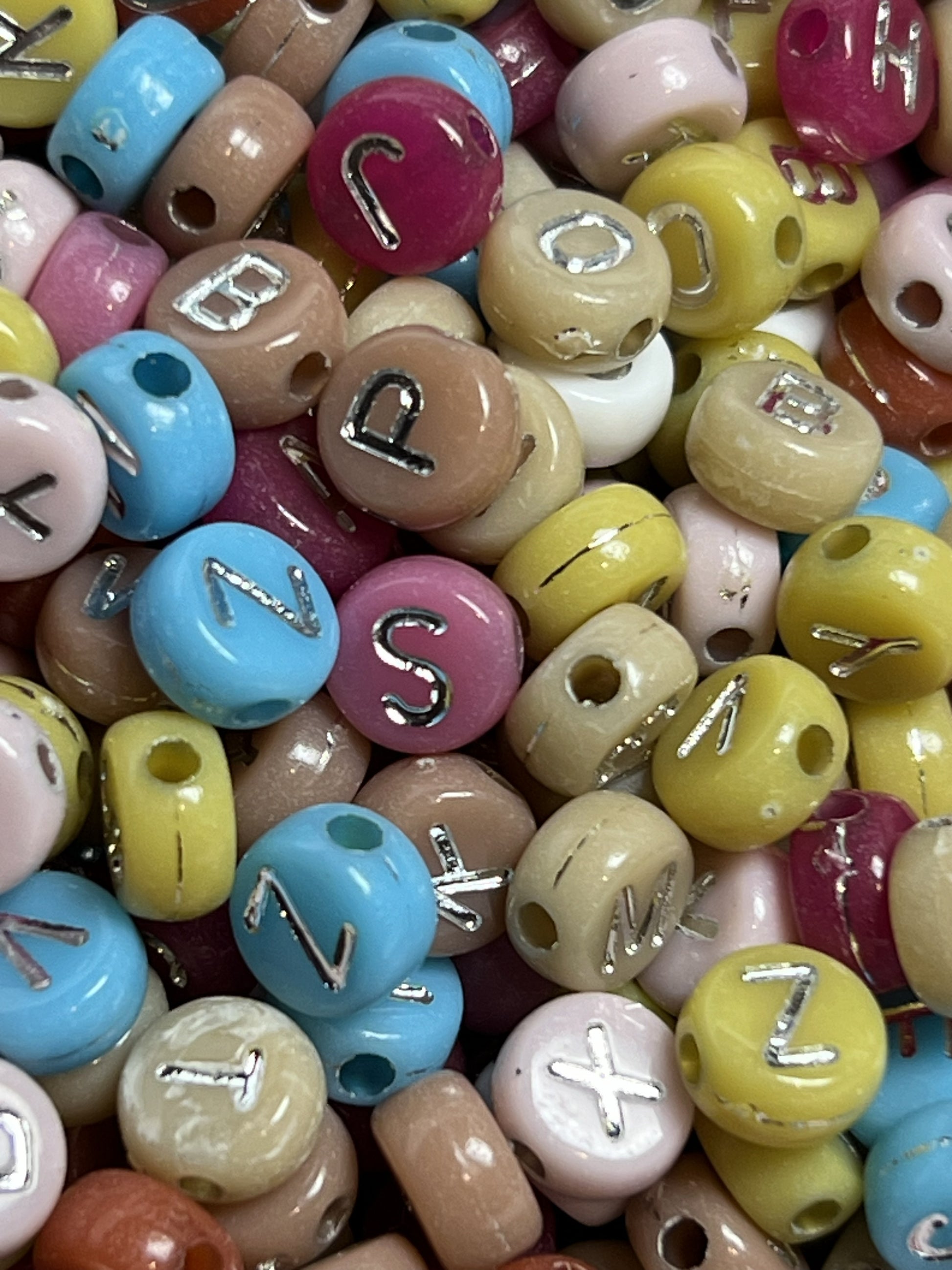 A pile of colorful acrylic beads featuring silver letters in a 7x4mm size.