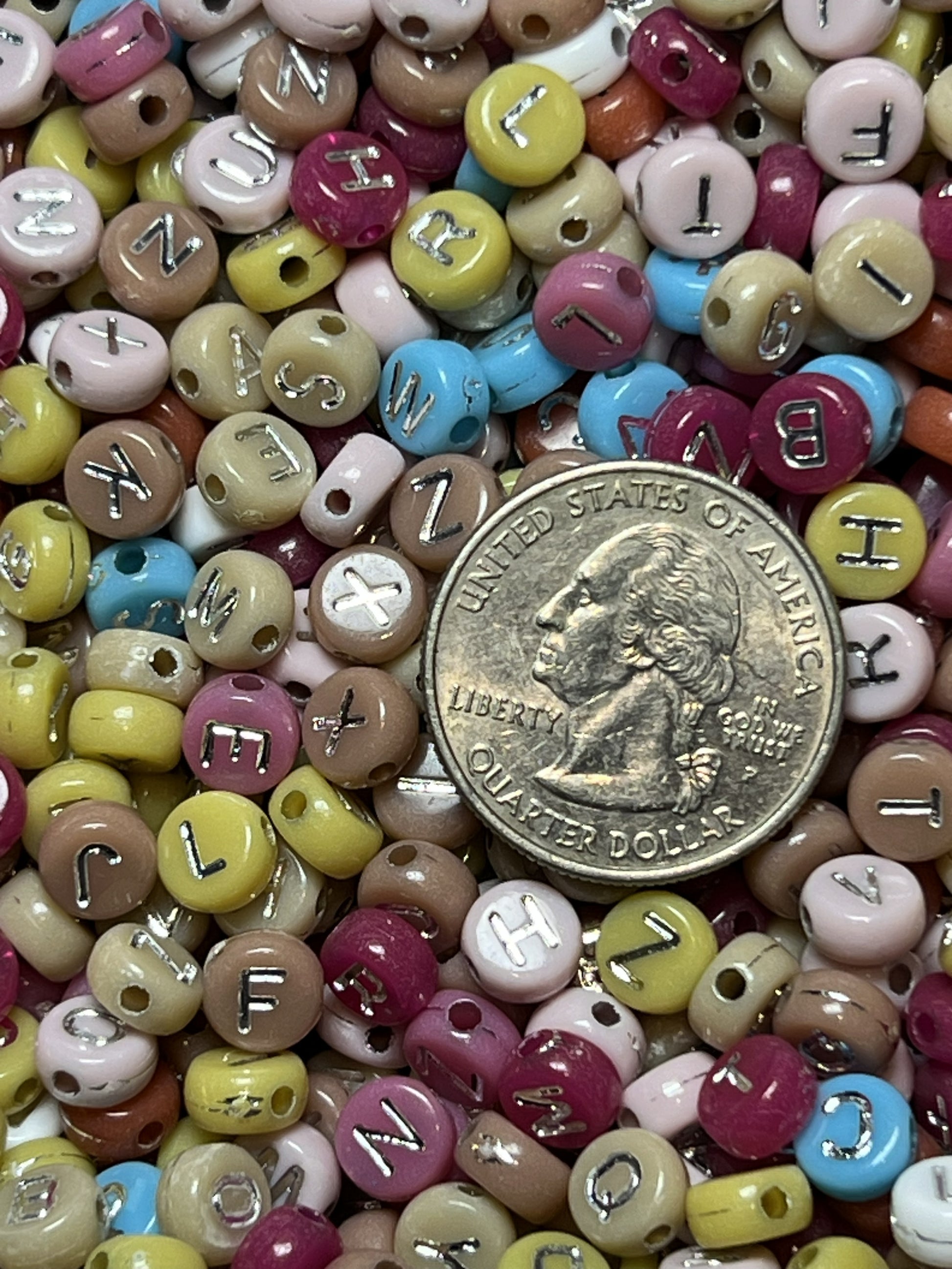 A pile of colorful acrylic beads with silver letters, shown next to a US quarter for scale.