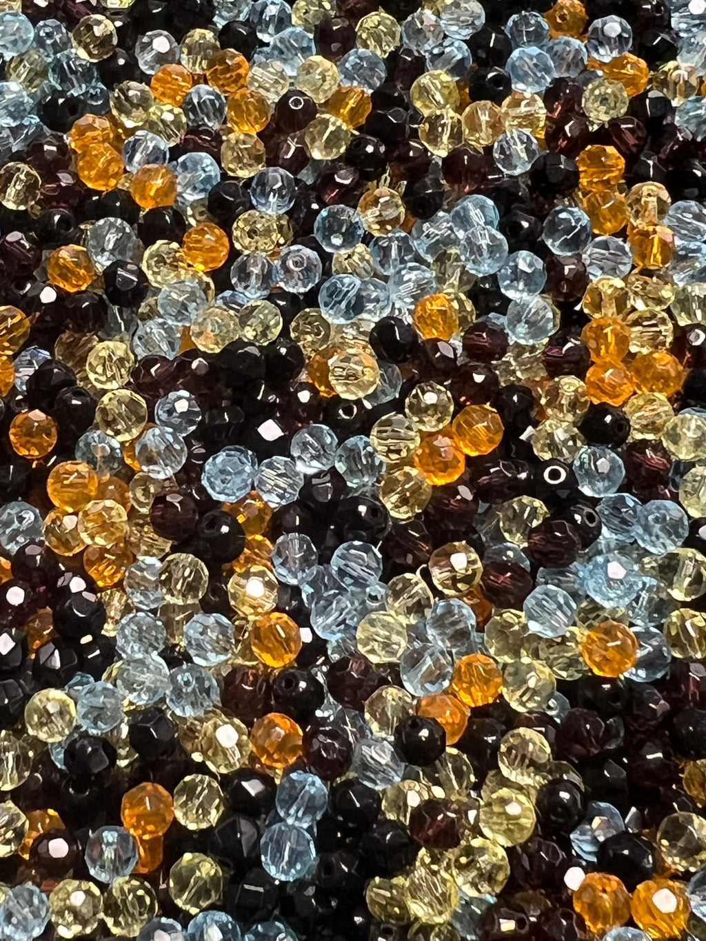 A pile of assorted 4mm faceted glass beads in shades of blue, yellow, orange, and dark brown.