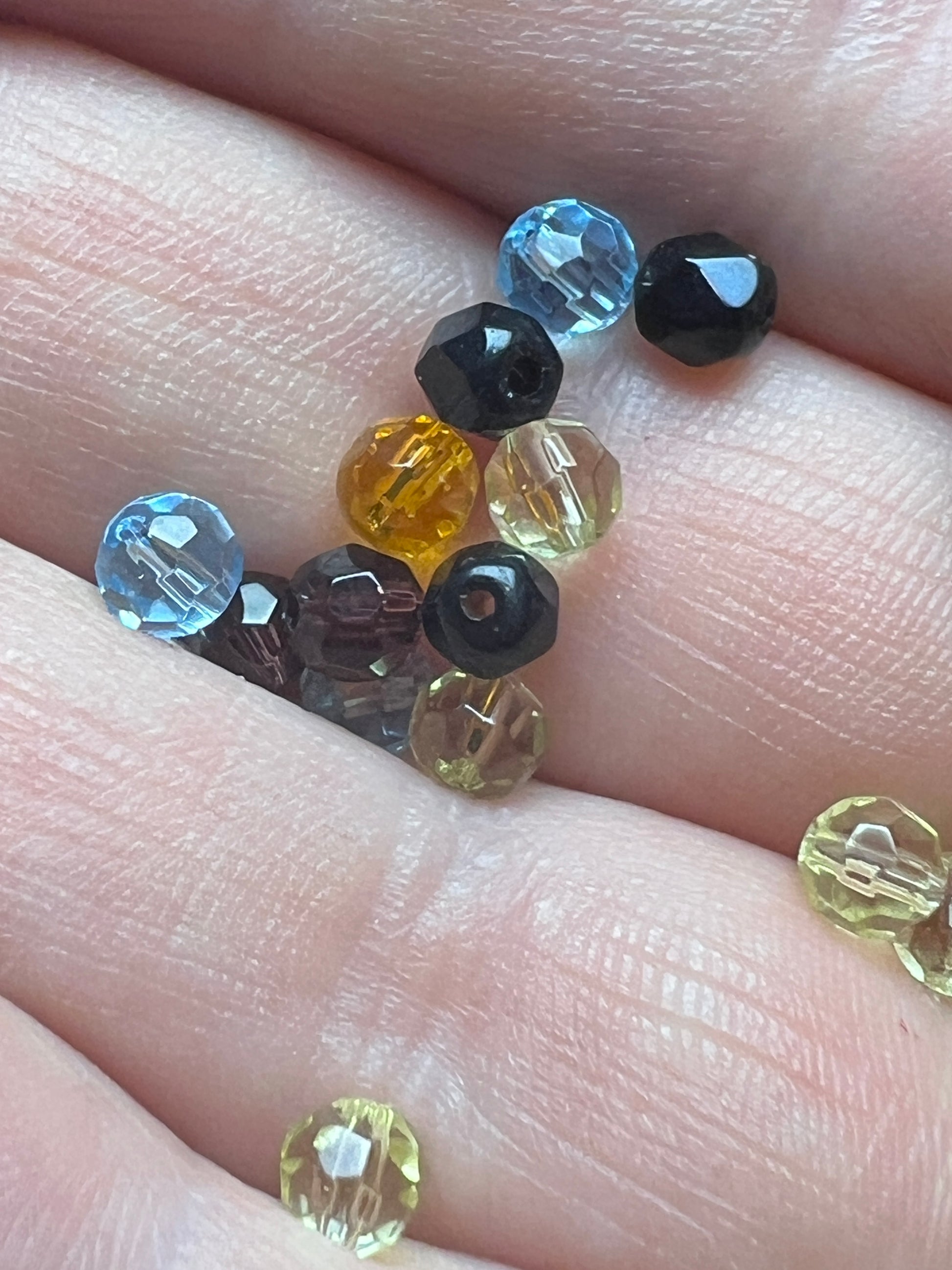 A handful of small, multicolored faceted glass beads resting on a person's palm.