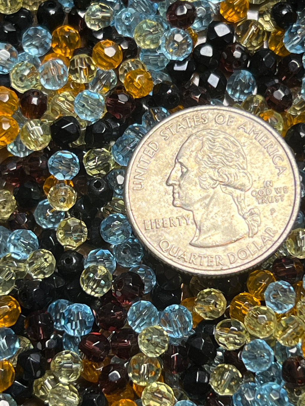 A pile of assorted 4mm faceted glass beads in blue, yellow, and black next to a US quarter.