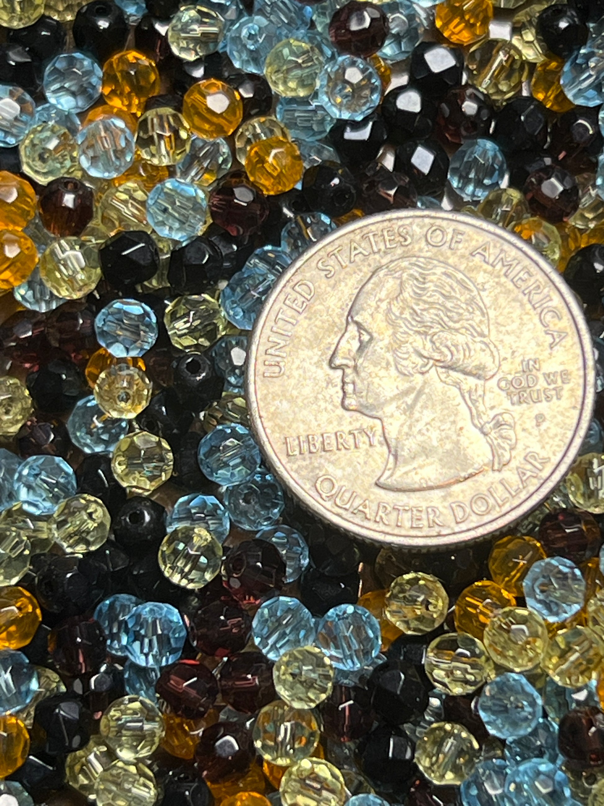A pile of assorted 4mm faceted glass beads in blue, yellow, and black next to a US quarter.