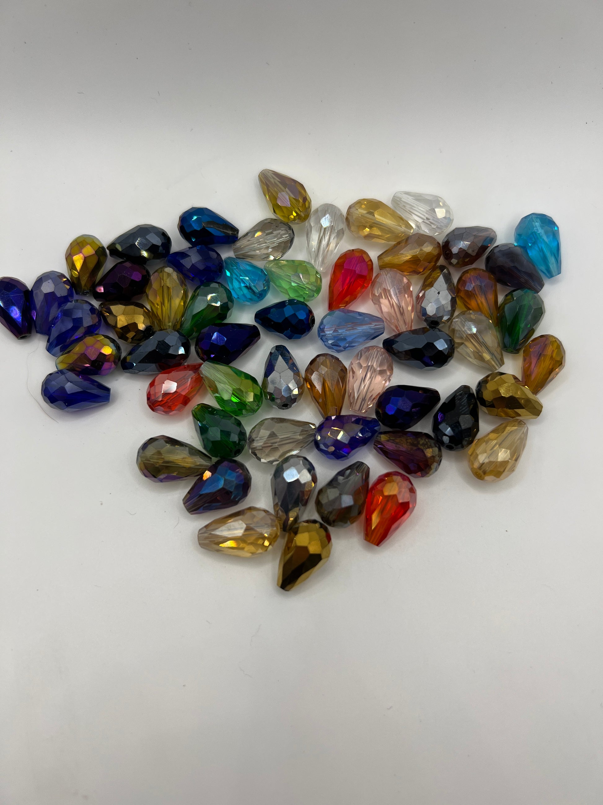 A collection of multicolored electroplated glass teardrop beads scattered on a white background.