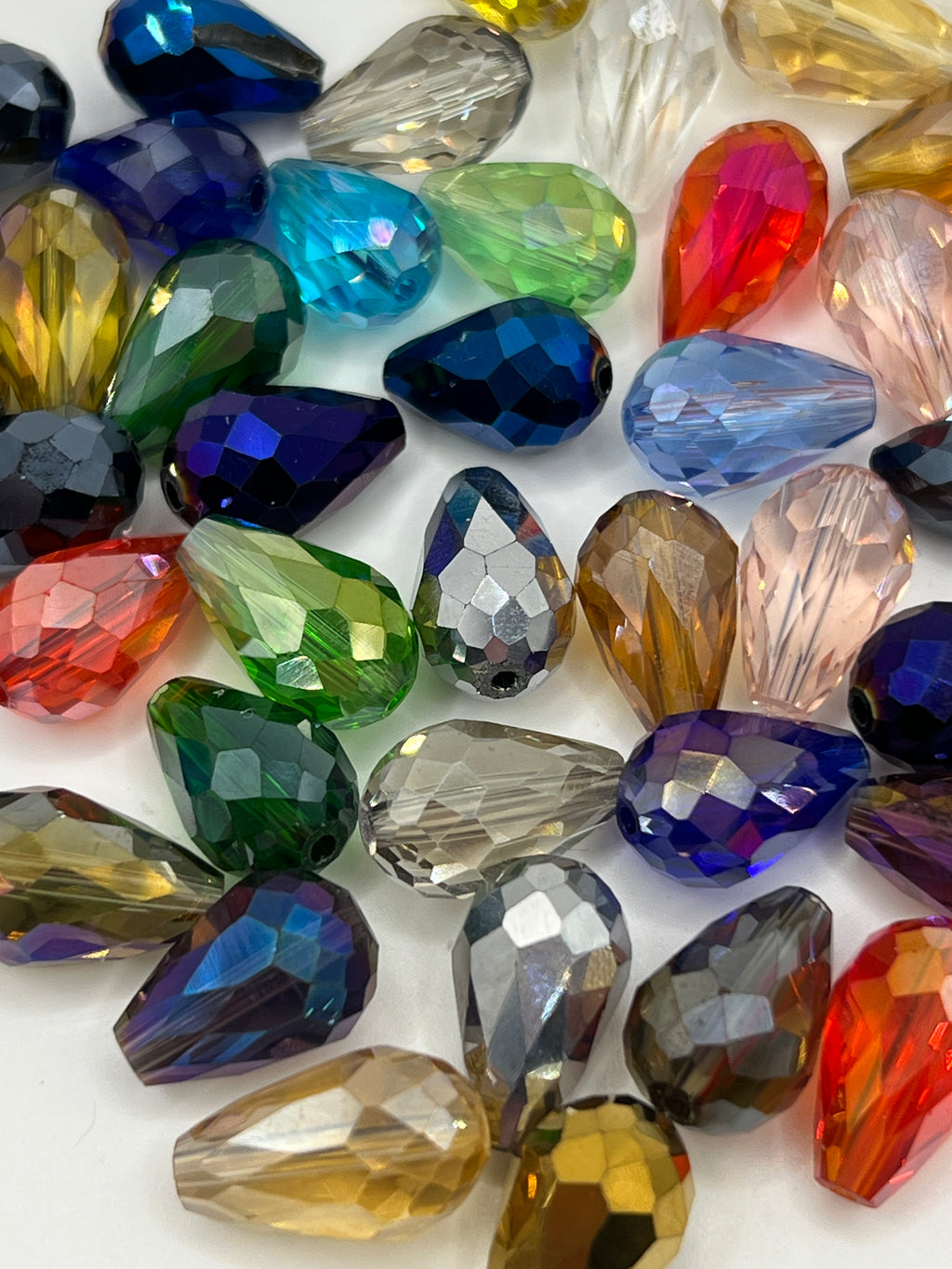 A collection of multicolored, faceted teardrop-shaped glass beads scattered on a white surface.
