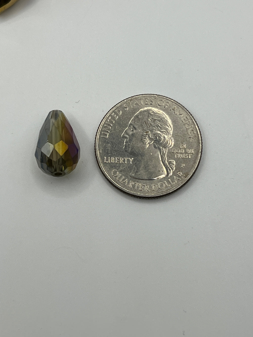 A single electroplated teardrop glass bead shown next to a US quarter for scale.