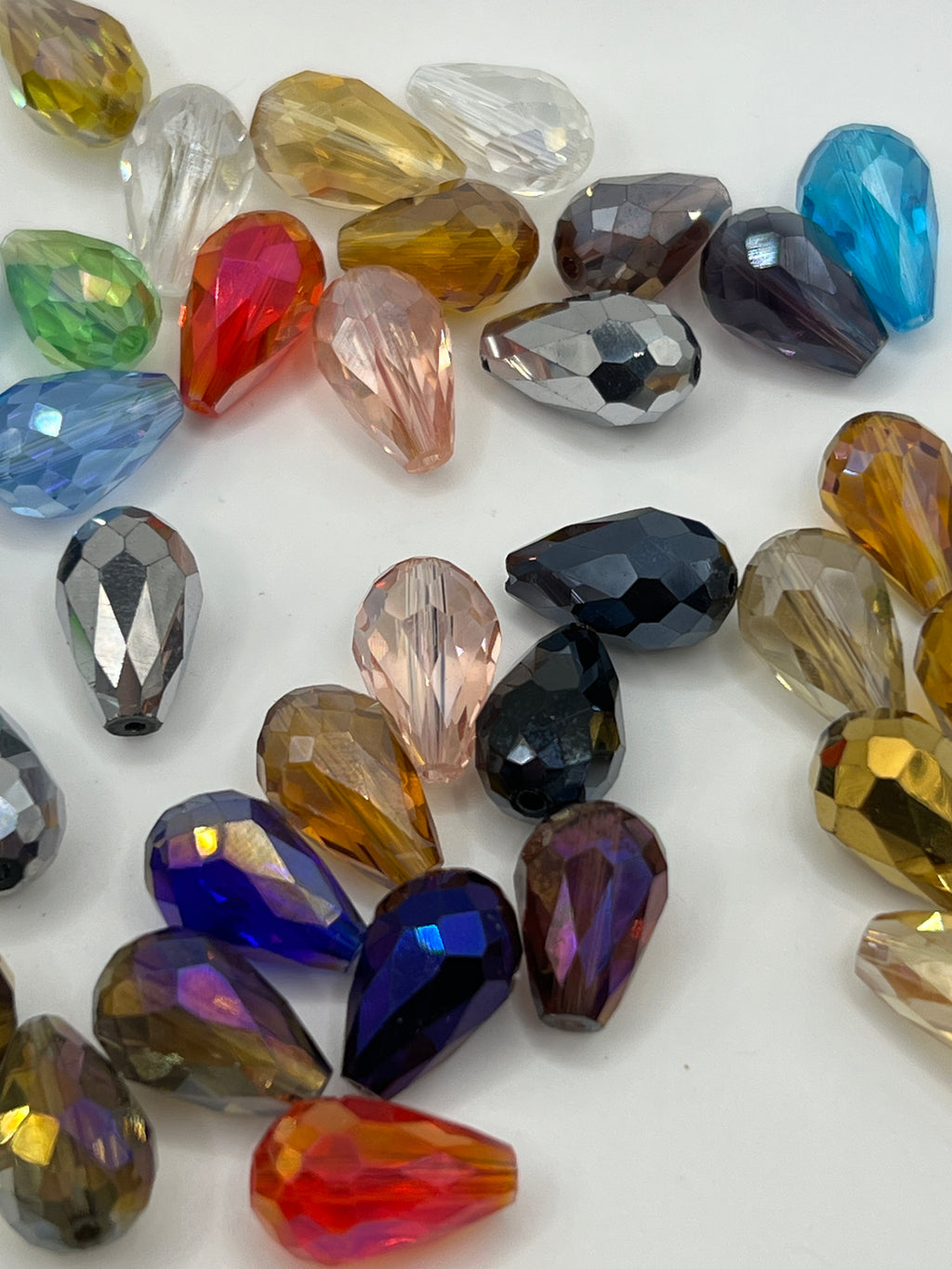 A collection of multicolored, faceted teardrop-shaped glass beads scattered on a white surface.