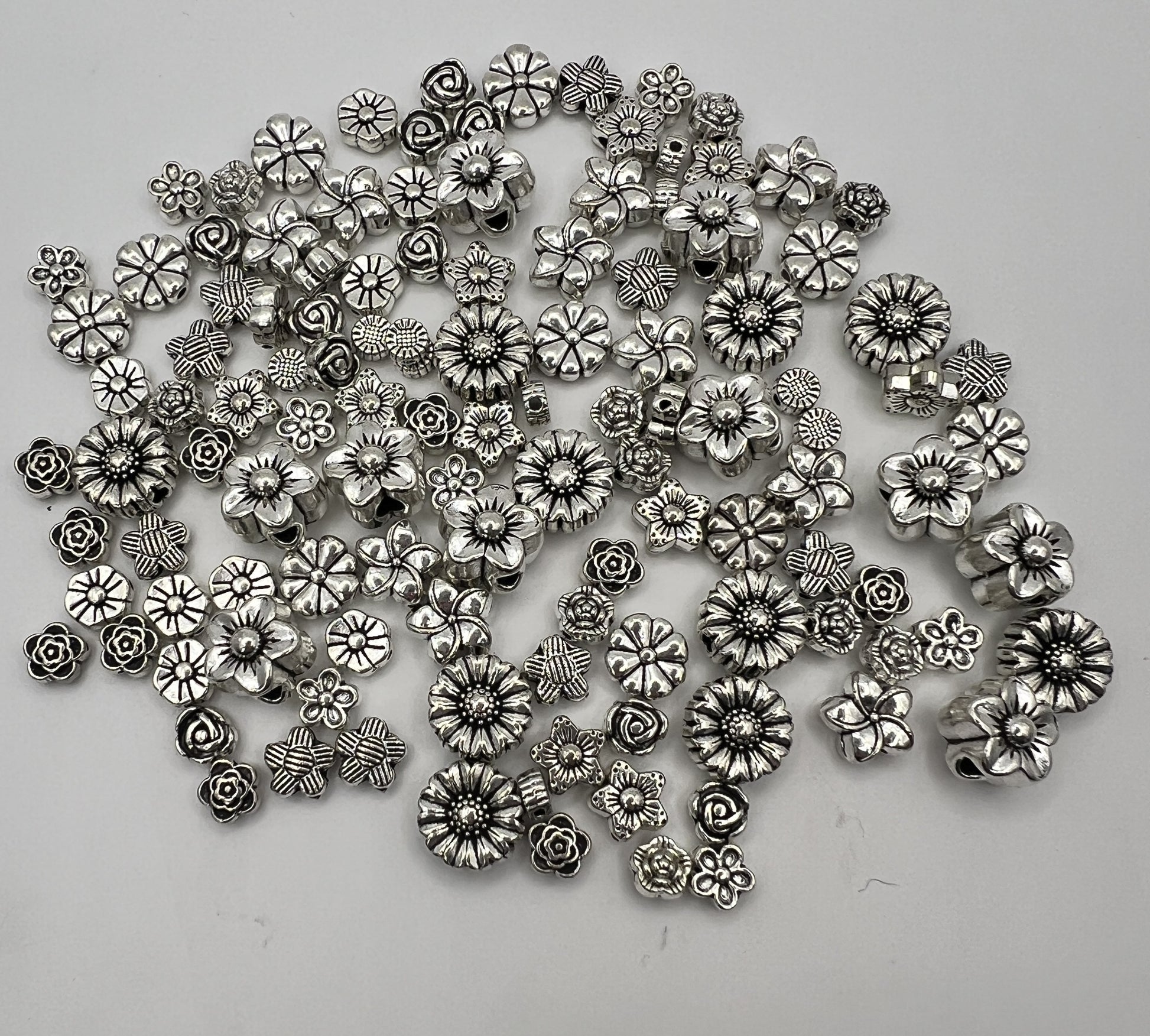 Assortment of 120 antique silver Tibetan style flower beads in various intricate floral designs.