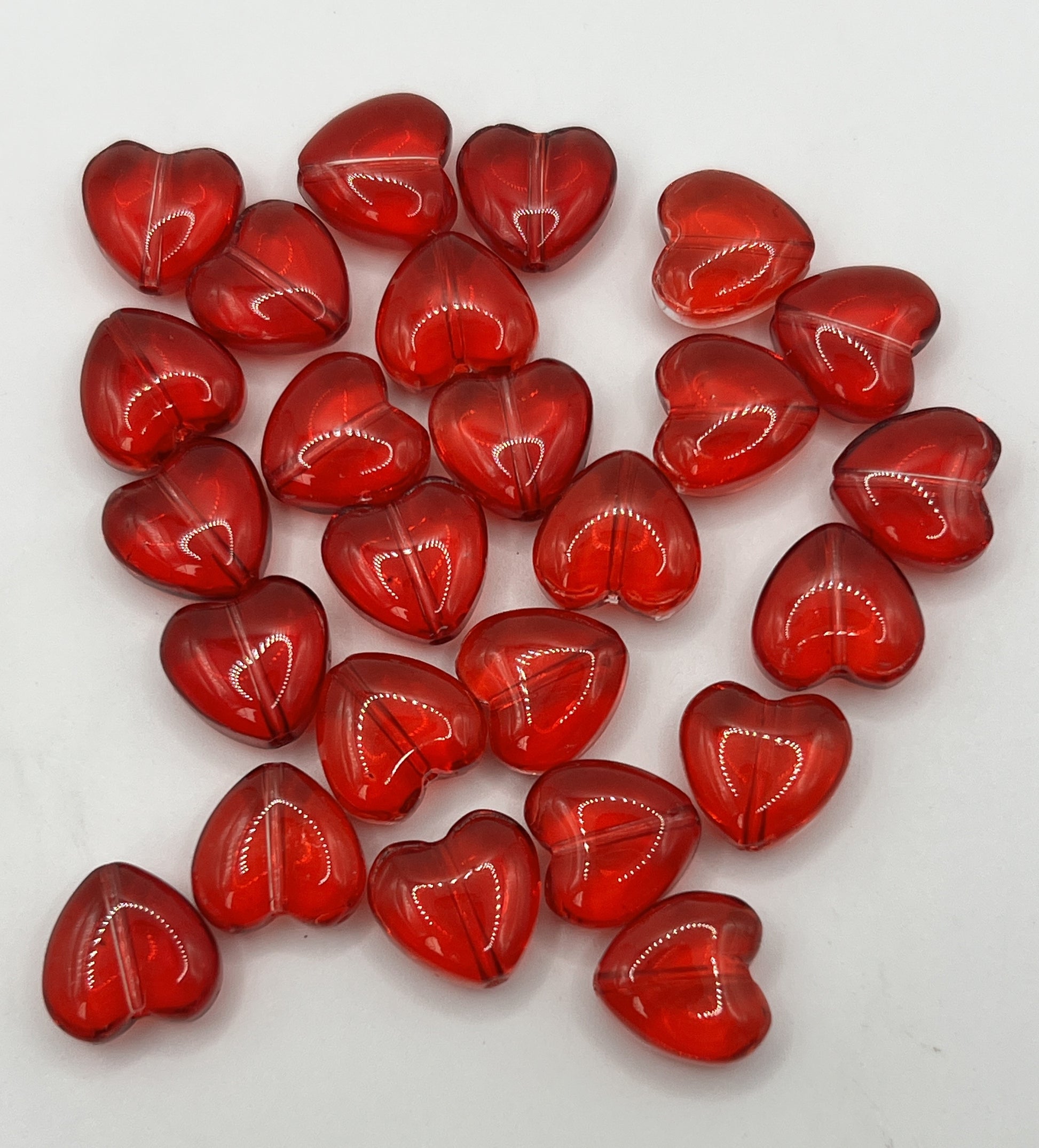 A collection of twenty-five transparent red glass heart-shaped beads on a white background.