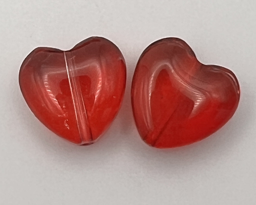 Two transparent red glass heart-shaped beads shown against a white background.