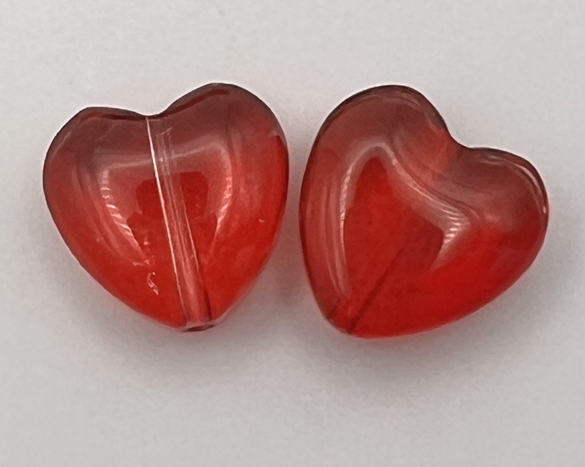Two transparent red glass heart-shaped beads shown against a white background.