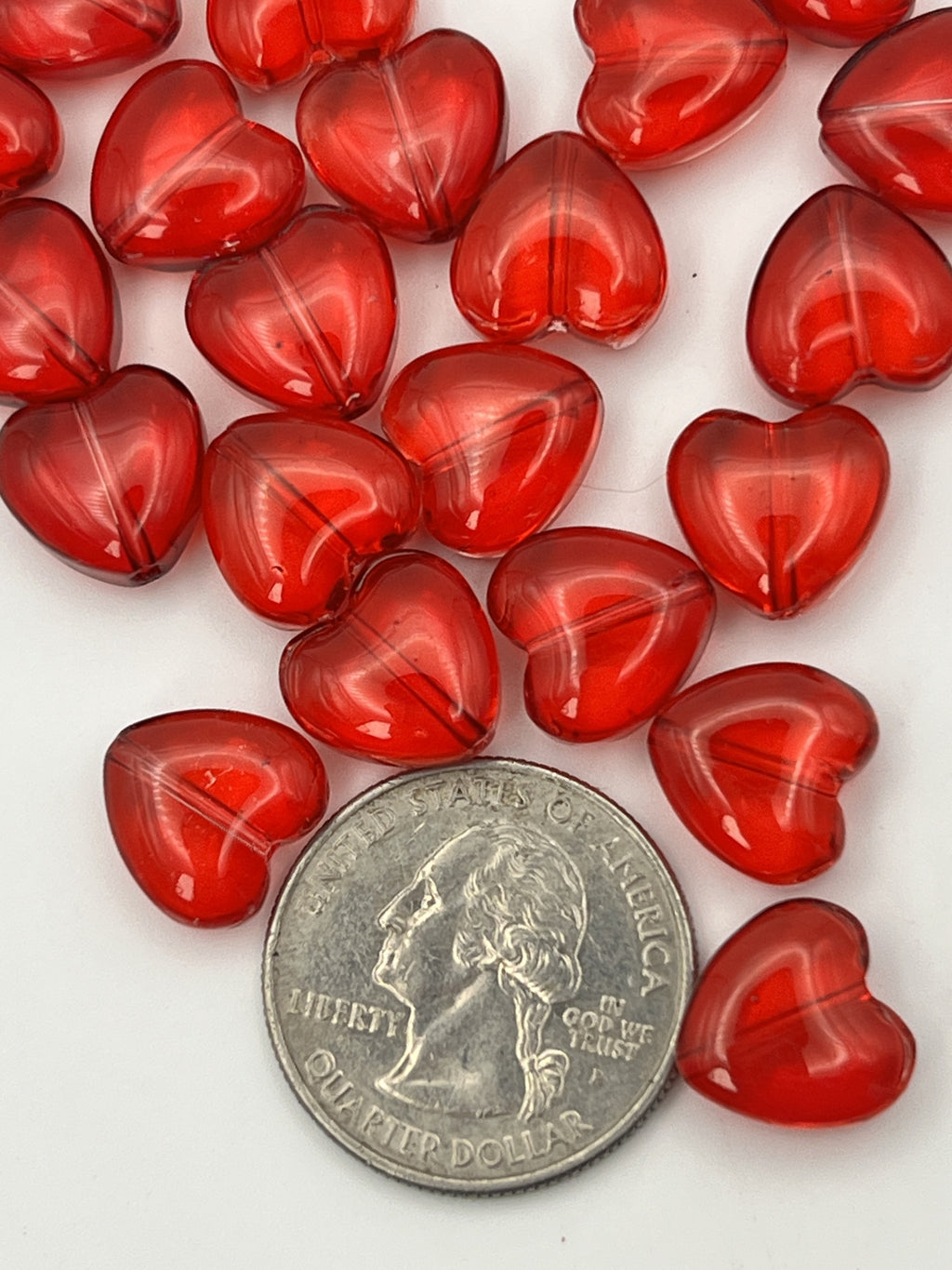 A collection of transparent red glass heart beads shown next to a US quarter for scale.
