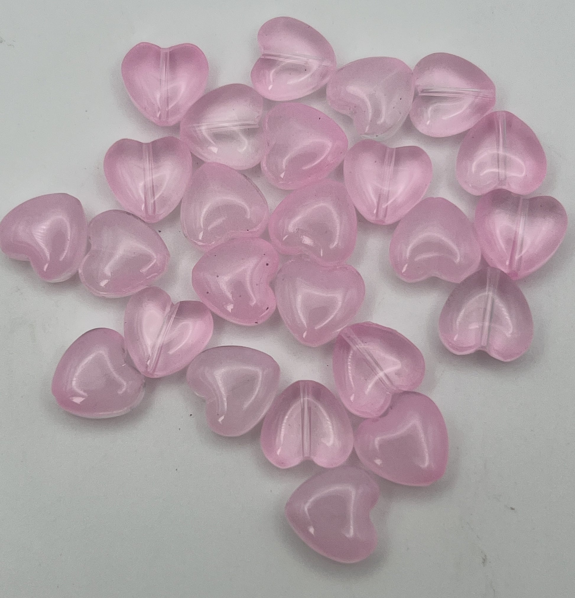 A collection of twenty-five translucent pearl pink glass heart beads for jewelry making.