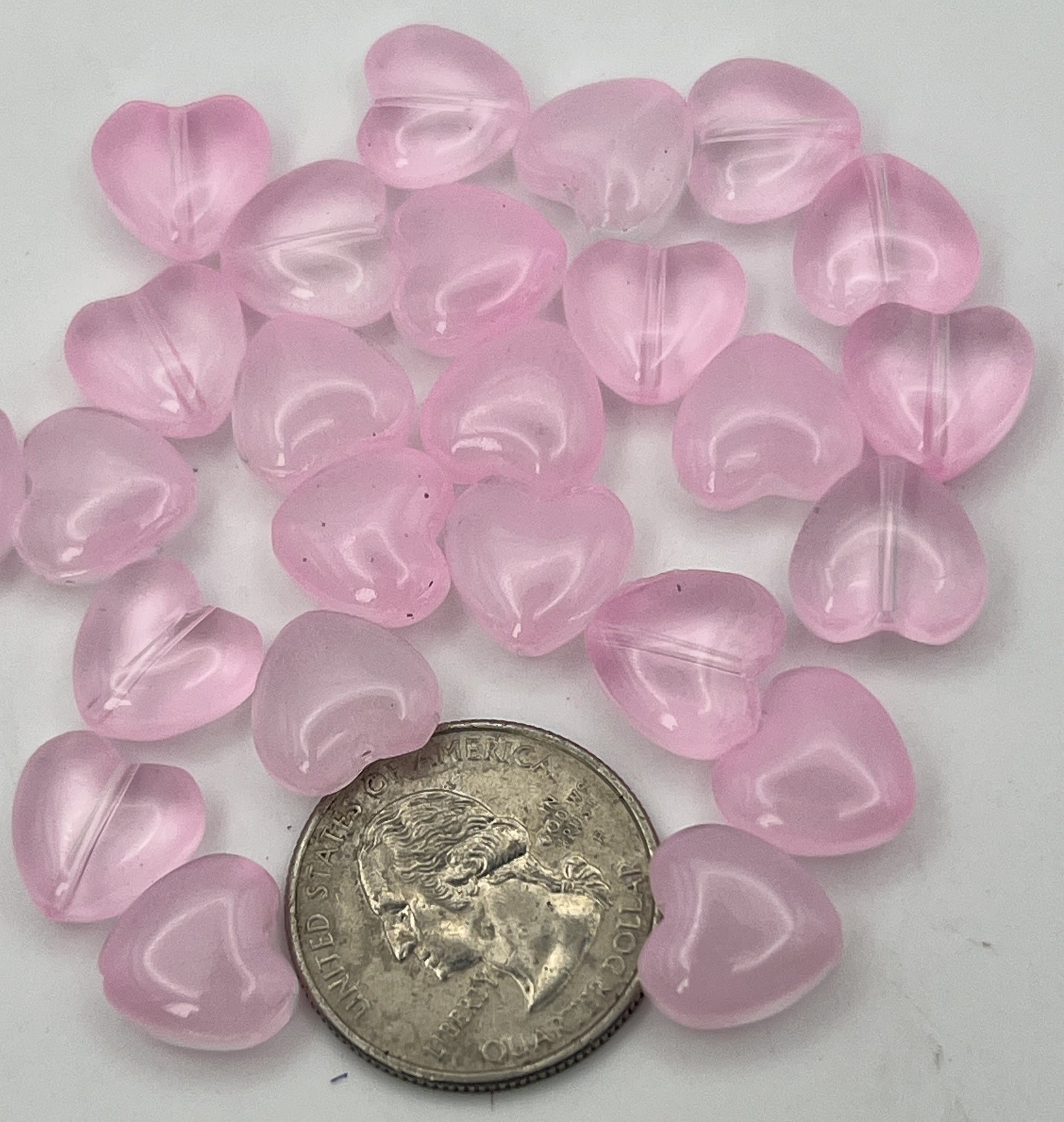 A pile of twenty-five transparent pearl pink glass heart beads next to a US quarter.