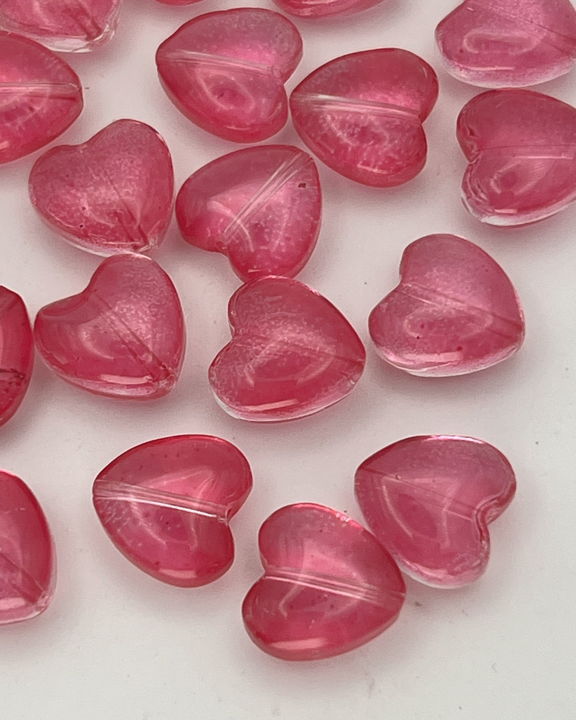 A collection of translucent camellia pink glass heart beads for jewelry making.