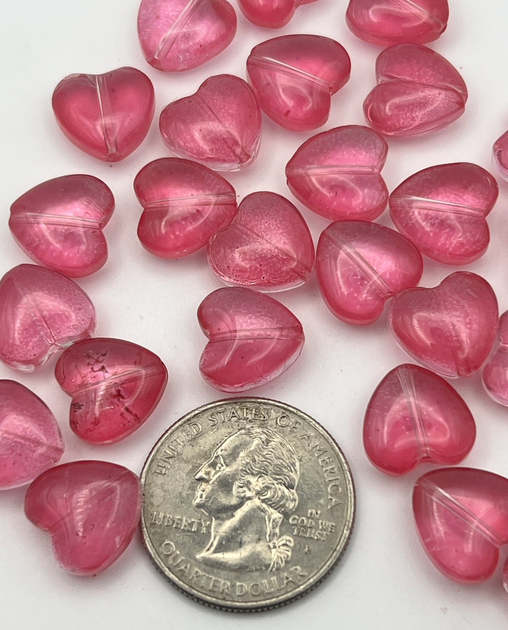 A collection of twenty-five translucent camellia pink glass heart beads shown next to a quarter.