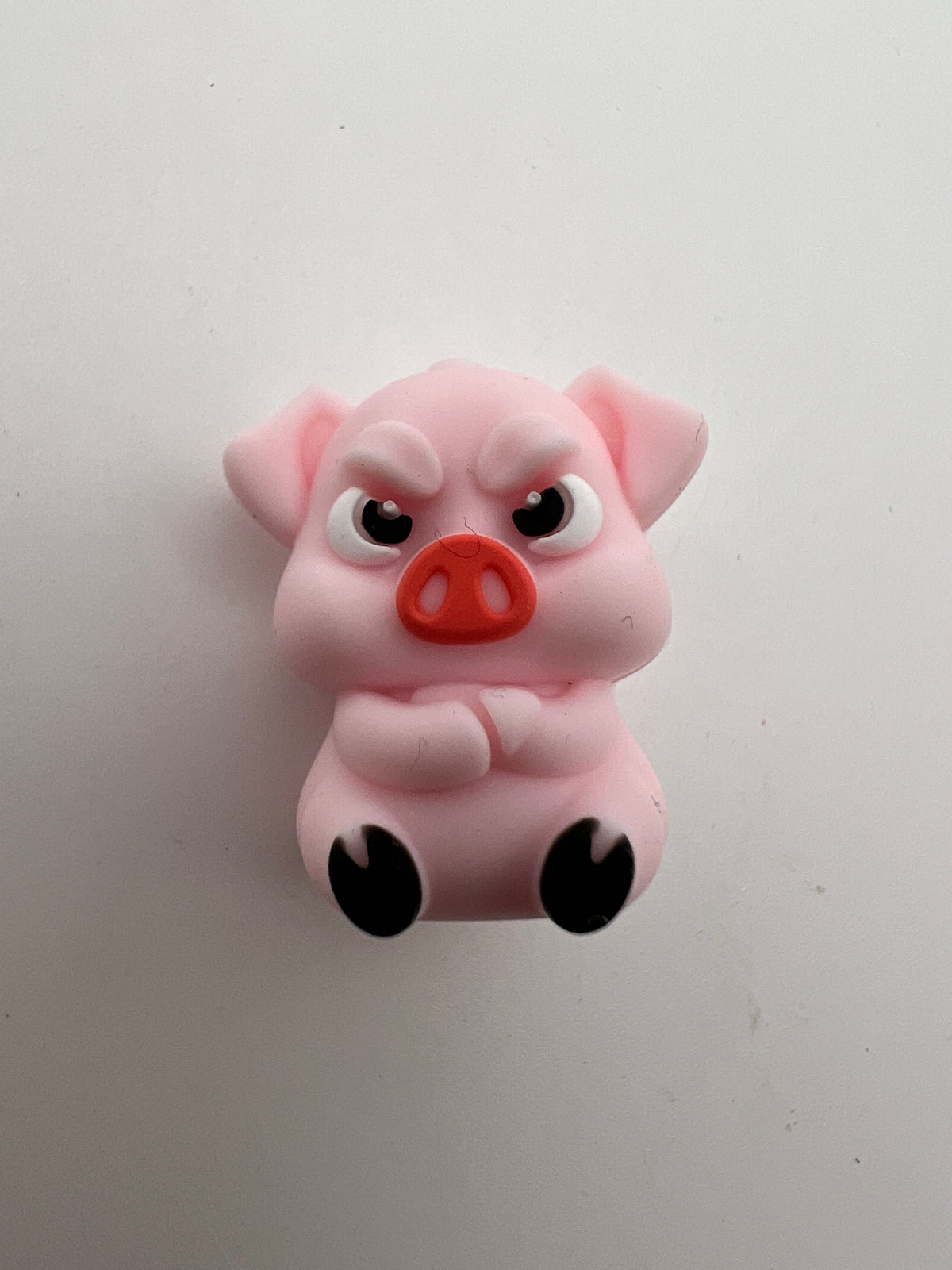Pink silicone focal bead shaped like a mad pig with an angry expression and black hooves.