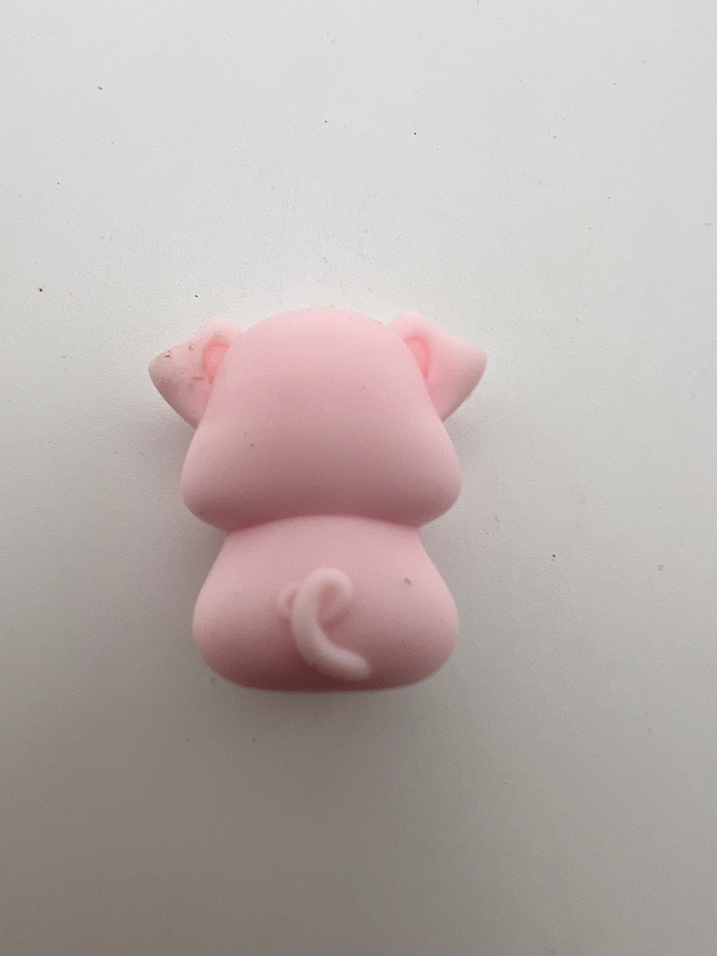 Back view of a pink silicone pig focal bead showing a curly tail and floppy ears.