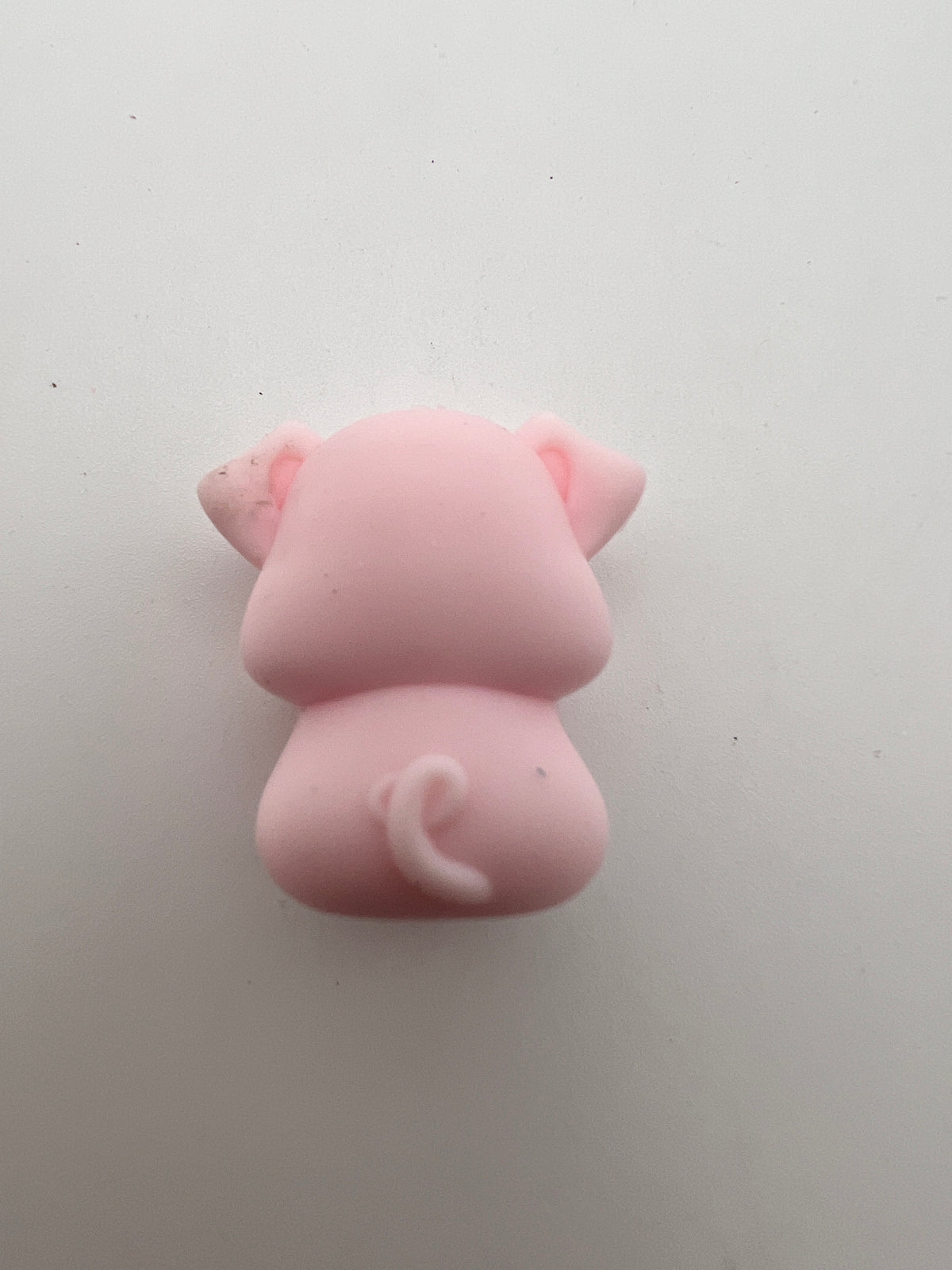 Back view of a pink silicone pig focal bead showing a curly tail and floppy ears.