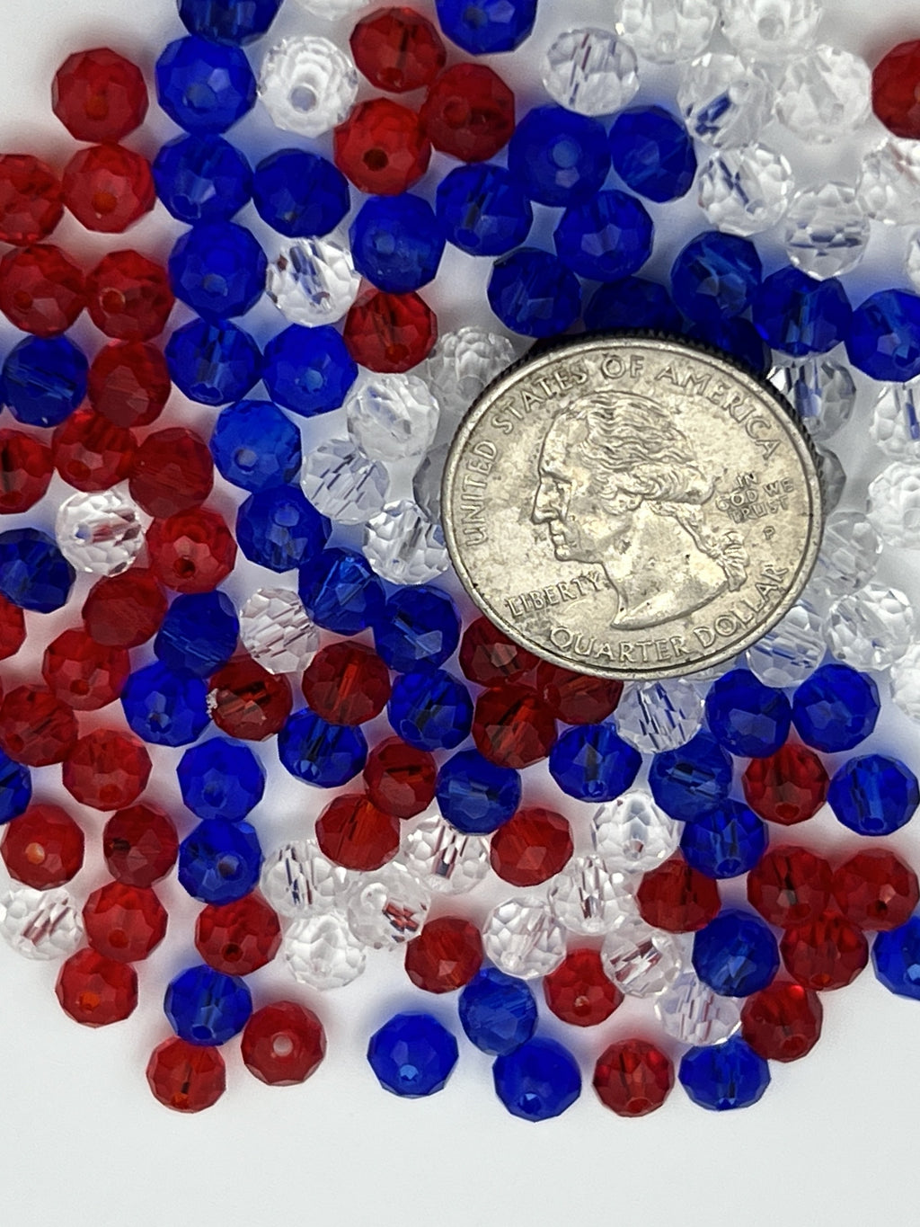 A pile of red, white, and blue faceted glass rondelle beads next to a US quarter.